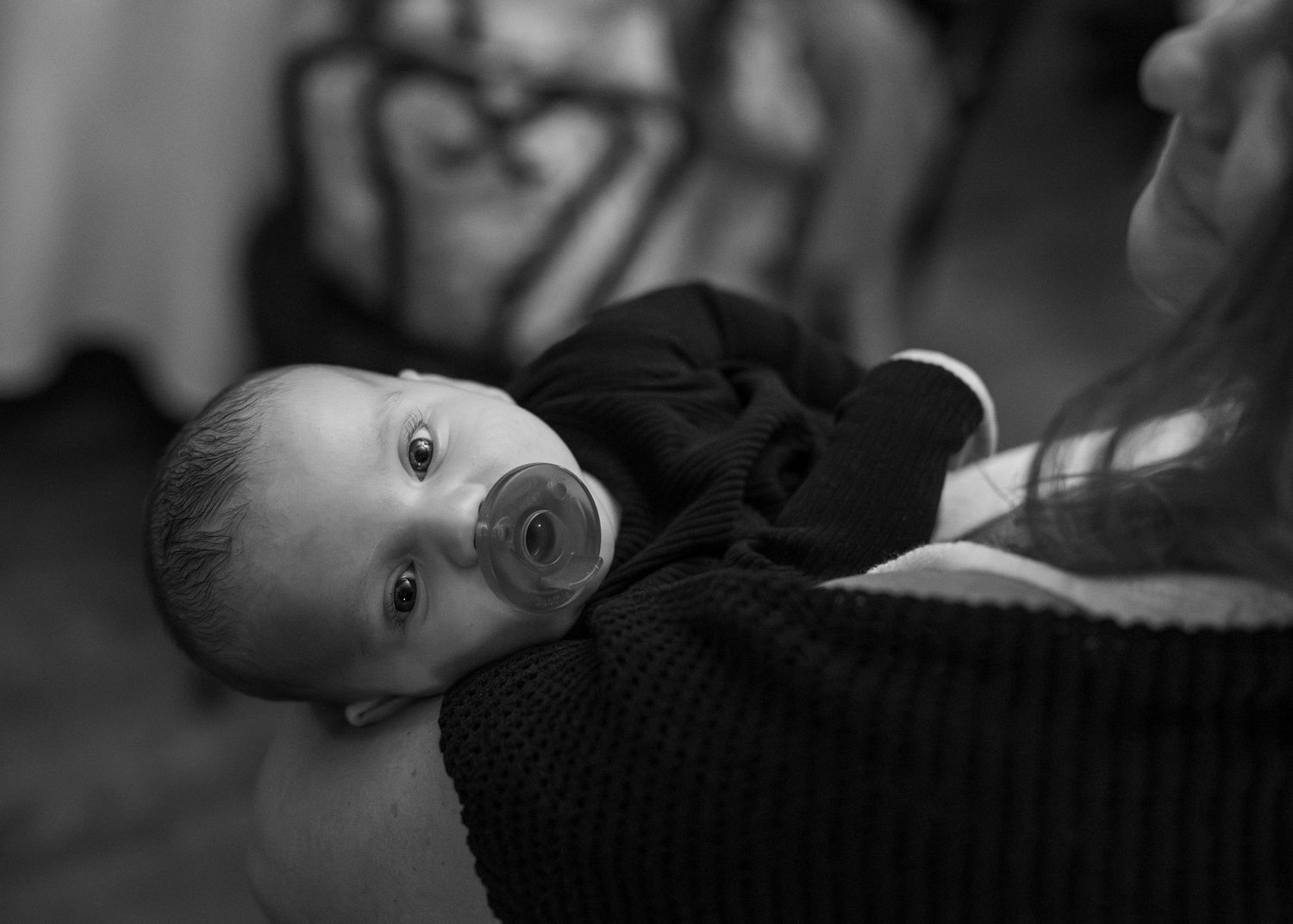 Black and white portrait of a baby in dark clothing looking up at the camera with bright eyes.