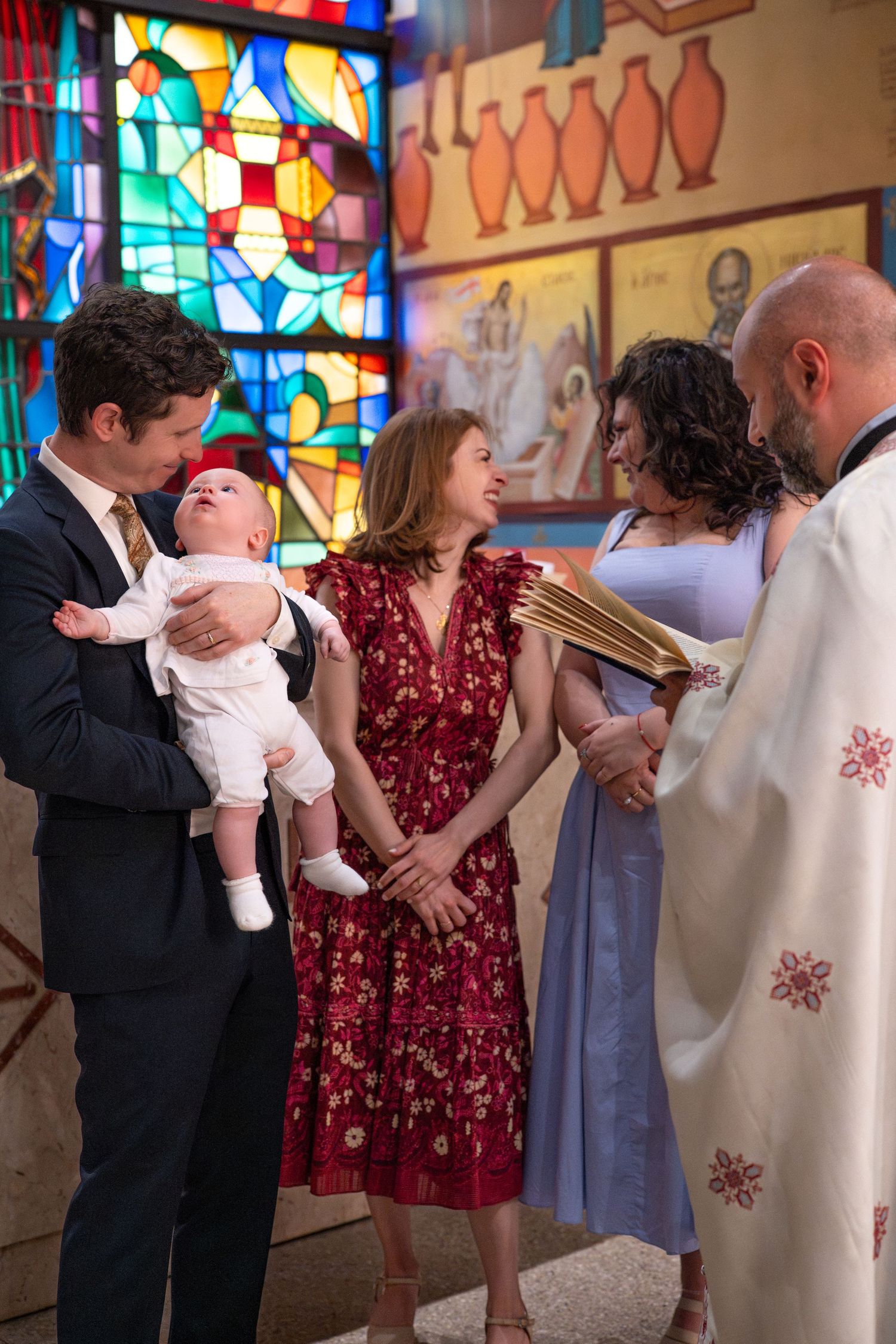 A baptism ceremony in progress inside a church with stained glass windows and traditional decor.