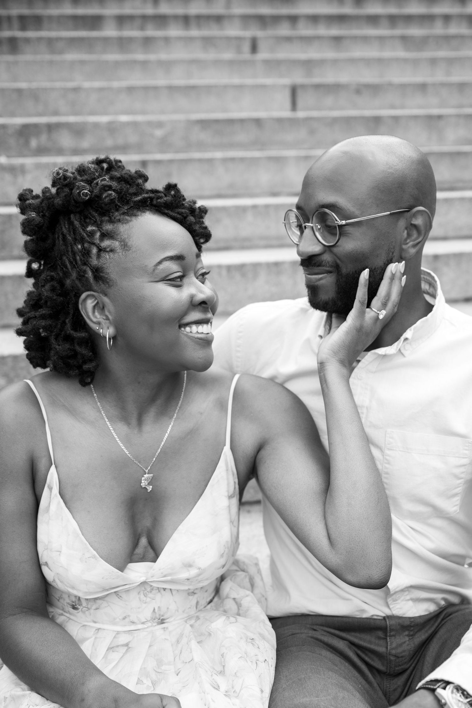A couple in coordinated white outfits shares candid laughter during an outdoor photoshoot.
