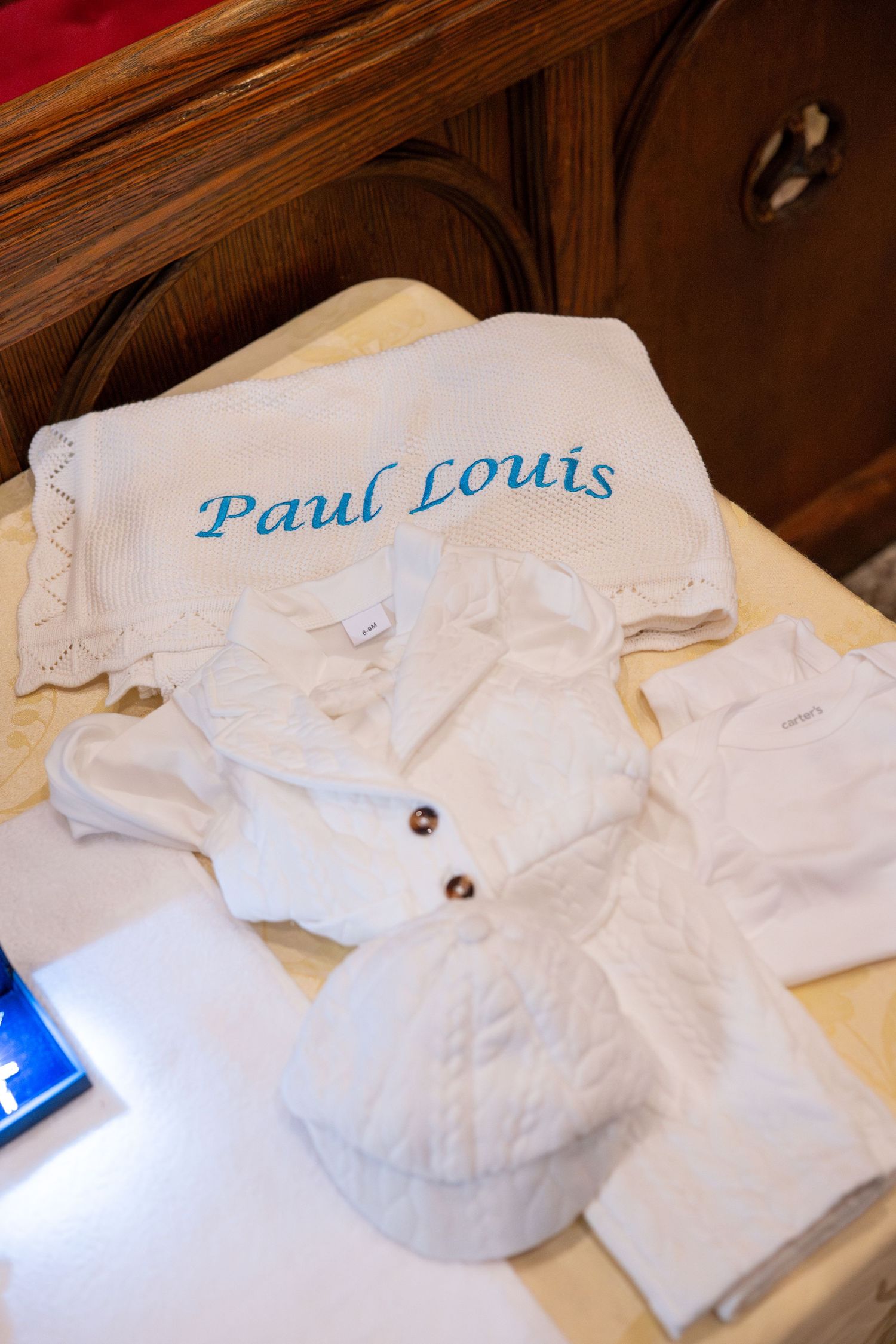 White baptismal gown with embroidered name laid flat on wooden surface.