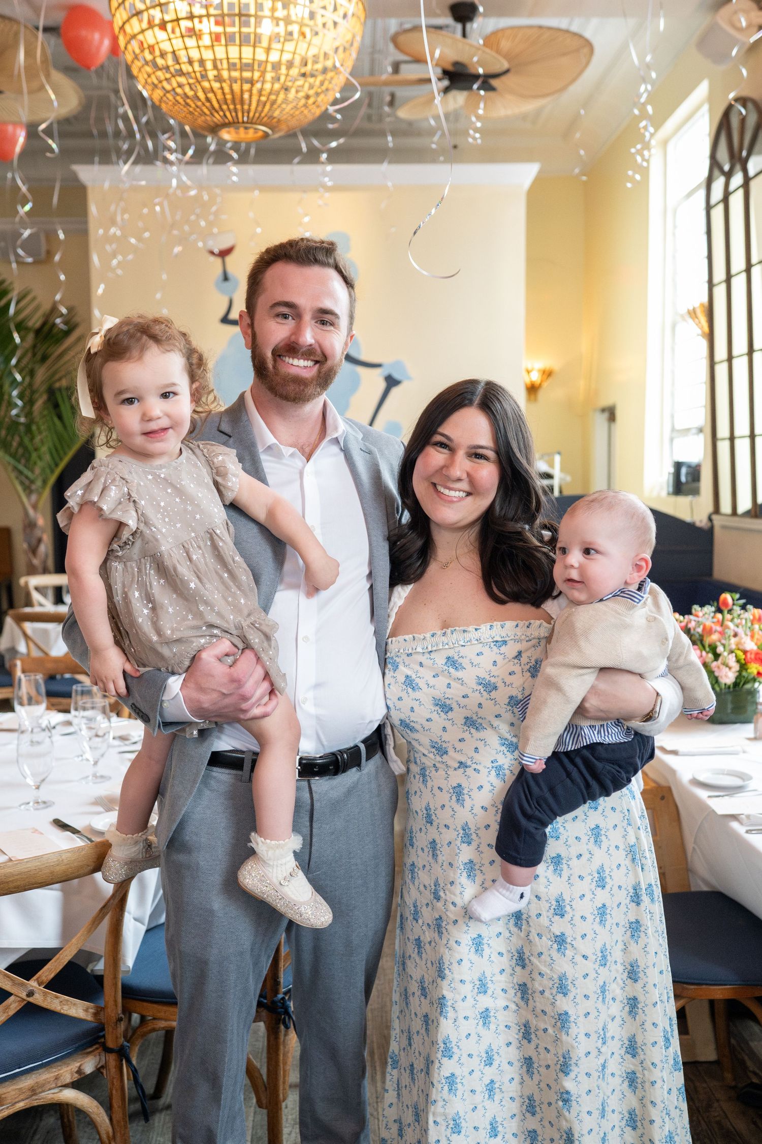 Happy family of four with two young children posing at celebration party in restaurant.