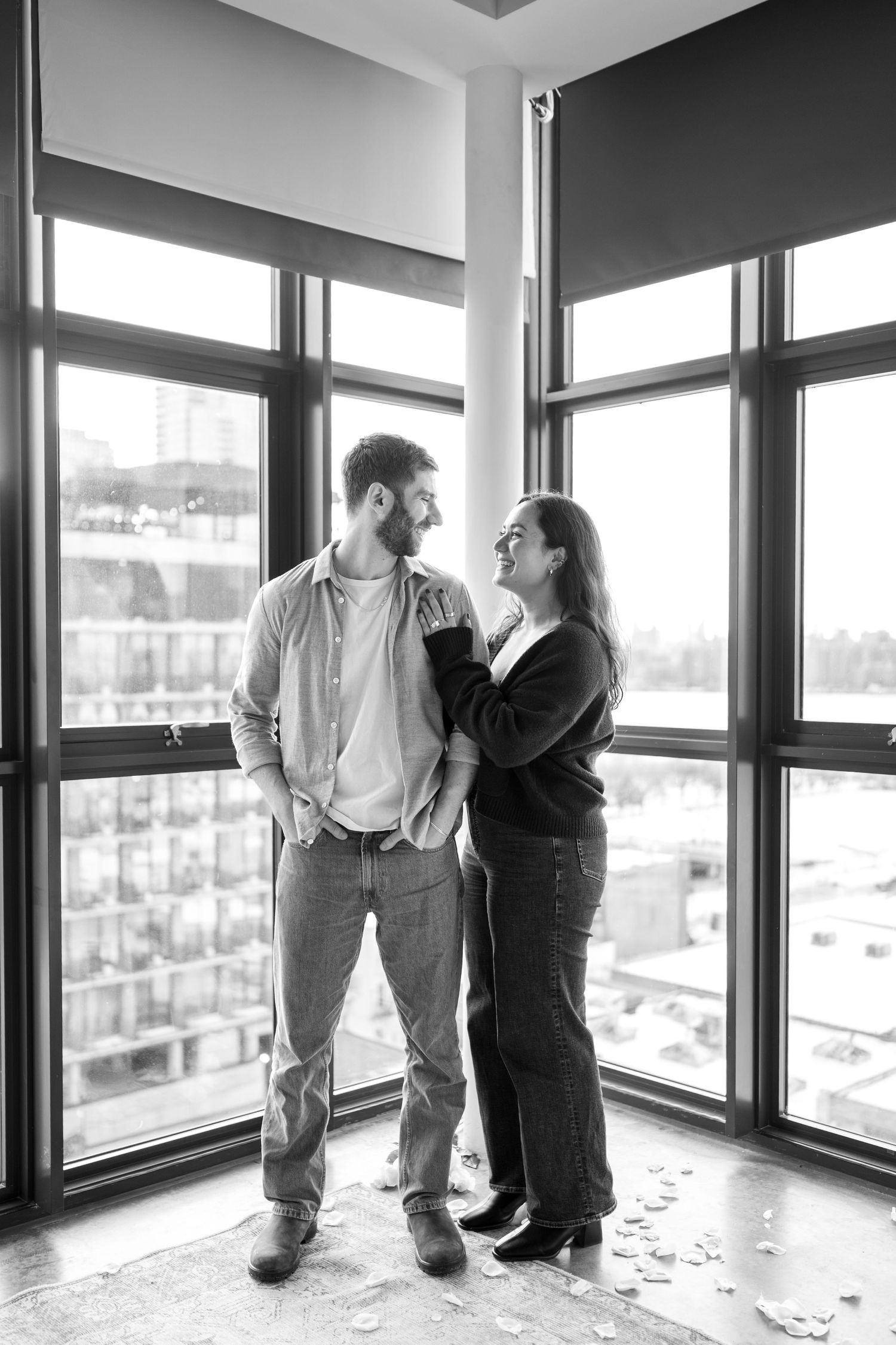 Black and white photo of people standing in a bright windowed room with a cityscape view.