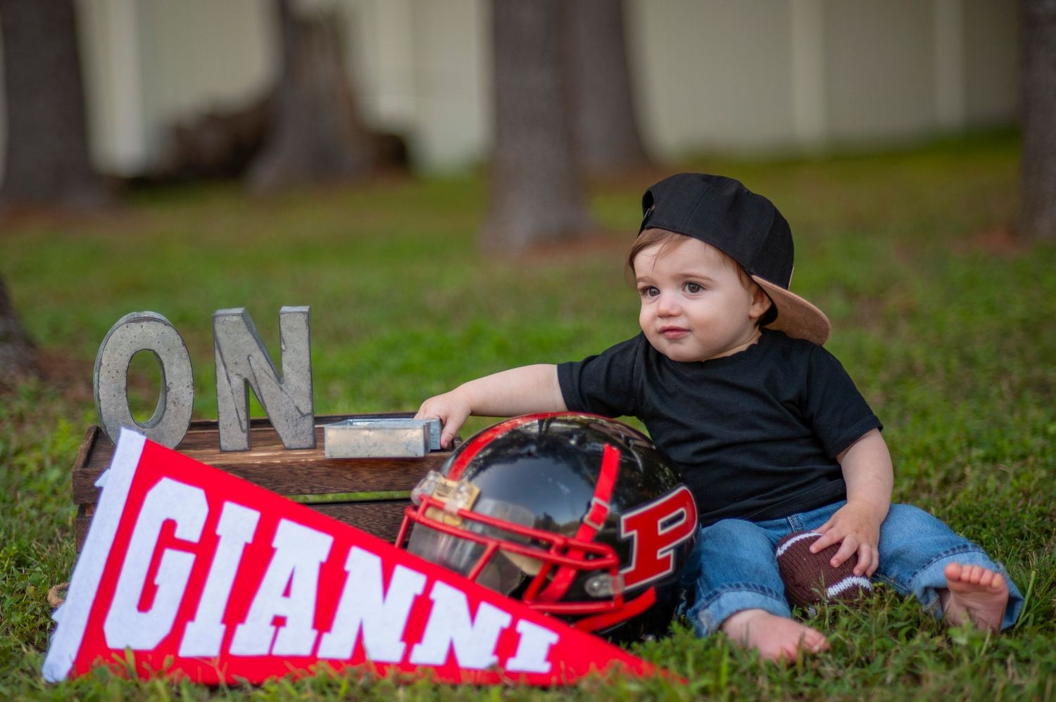 Baby wearing baseball cap sits with Giants banner and baseball glove outdoors.