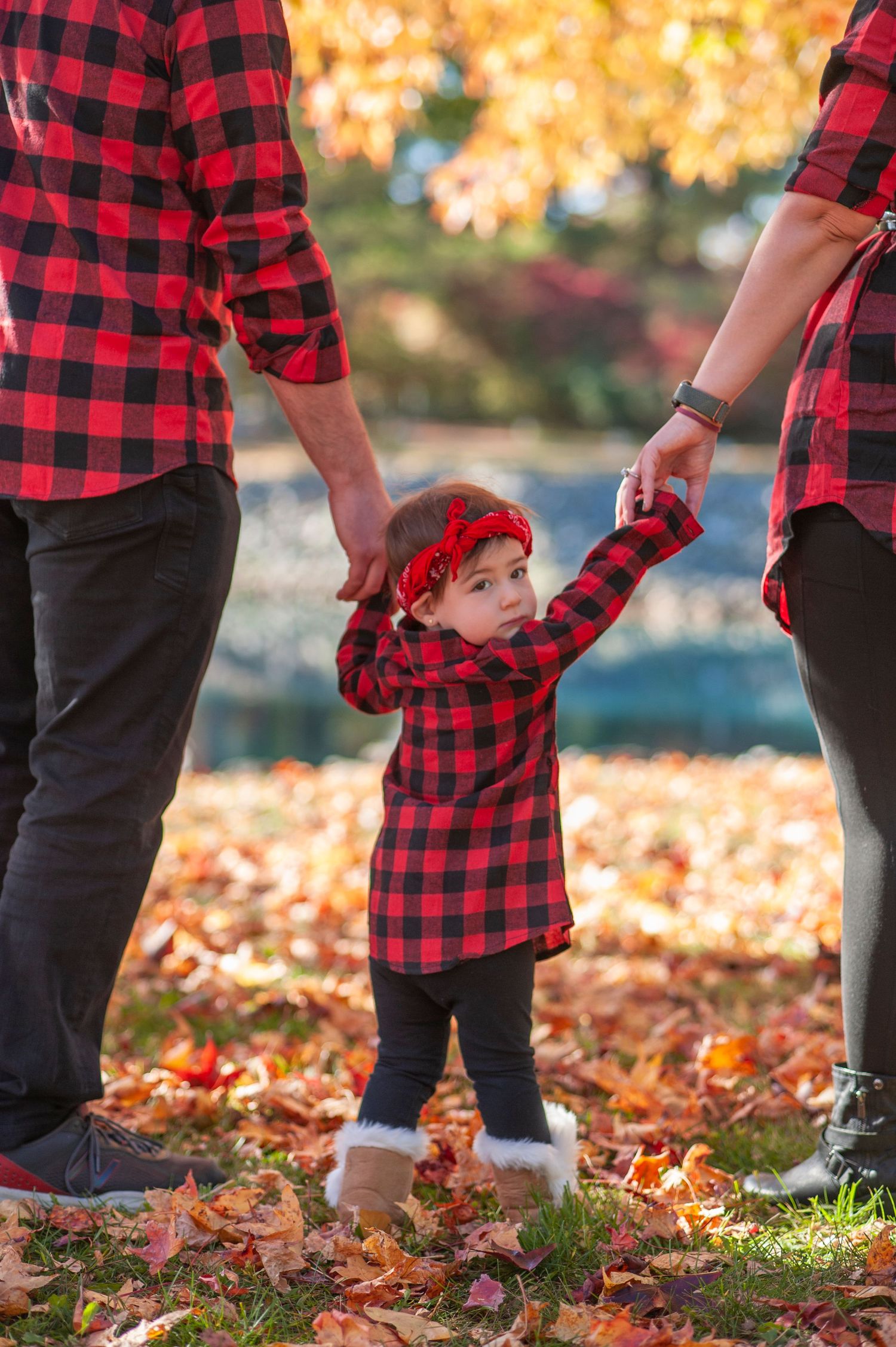 Family wearing matching red and black buffalo plaid shirts stand together in autumn leaves during golden hour.