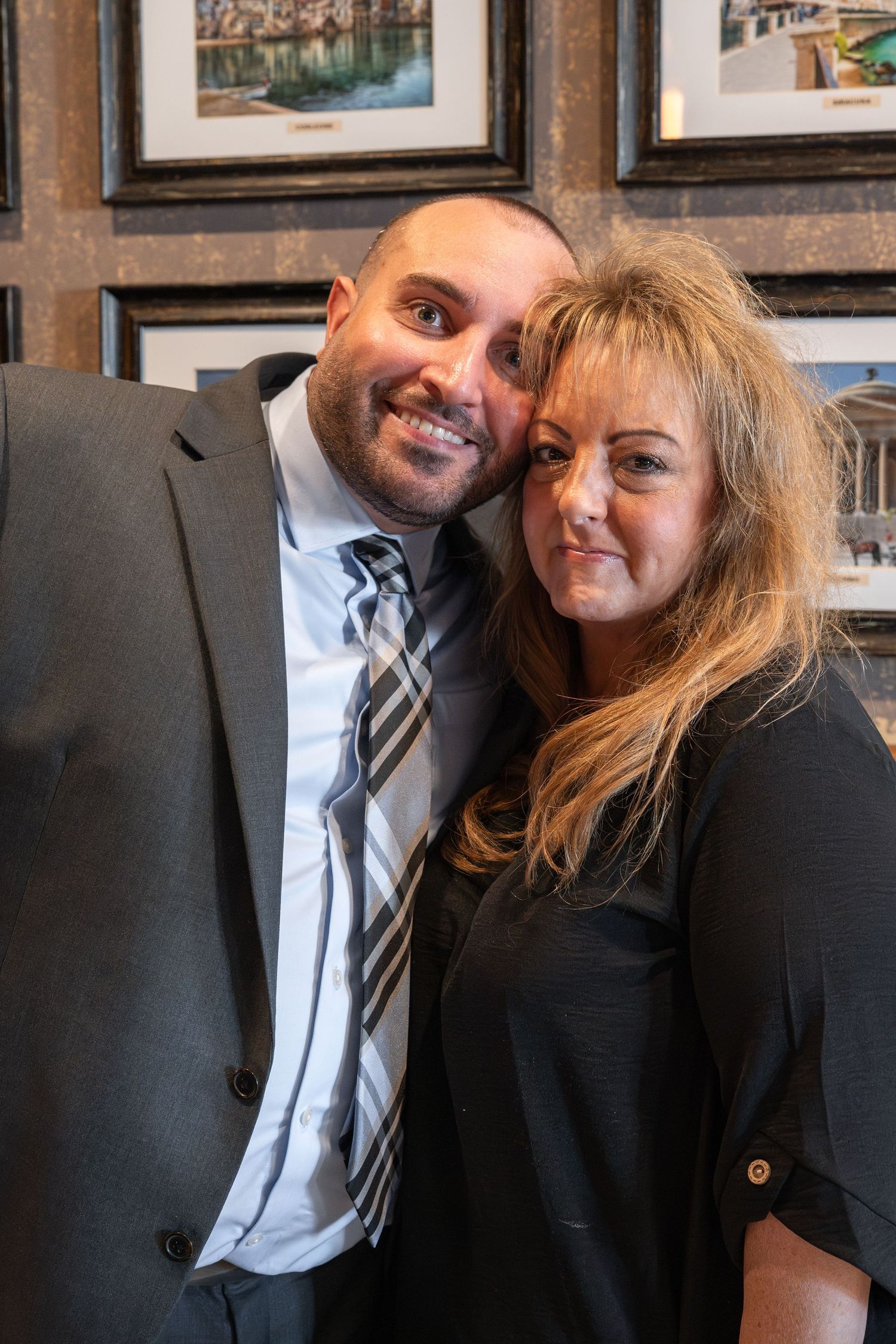 A couple in formal attire share an intimate moment while seated in front of framed artwork.