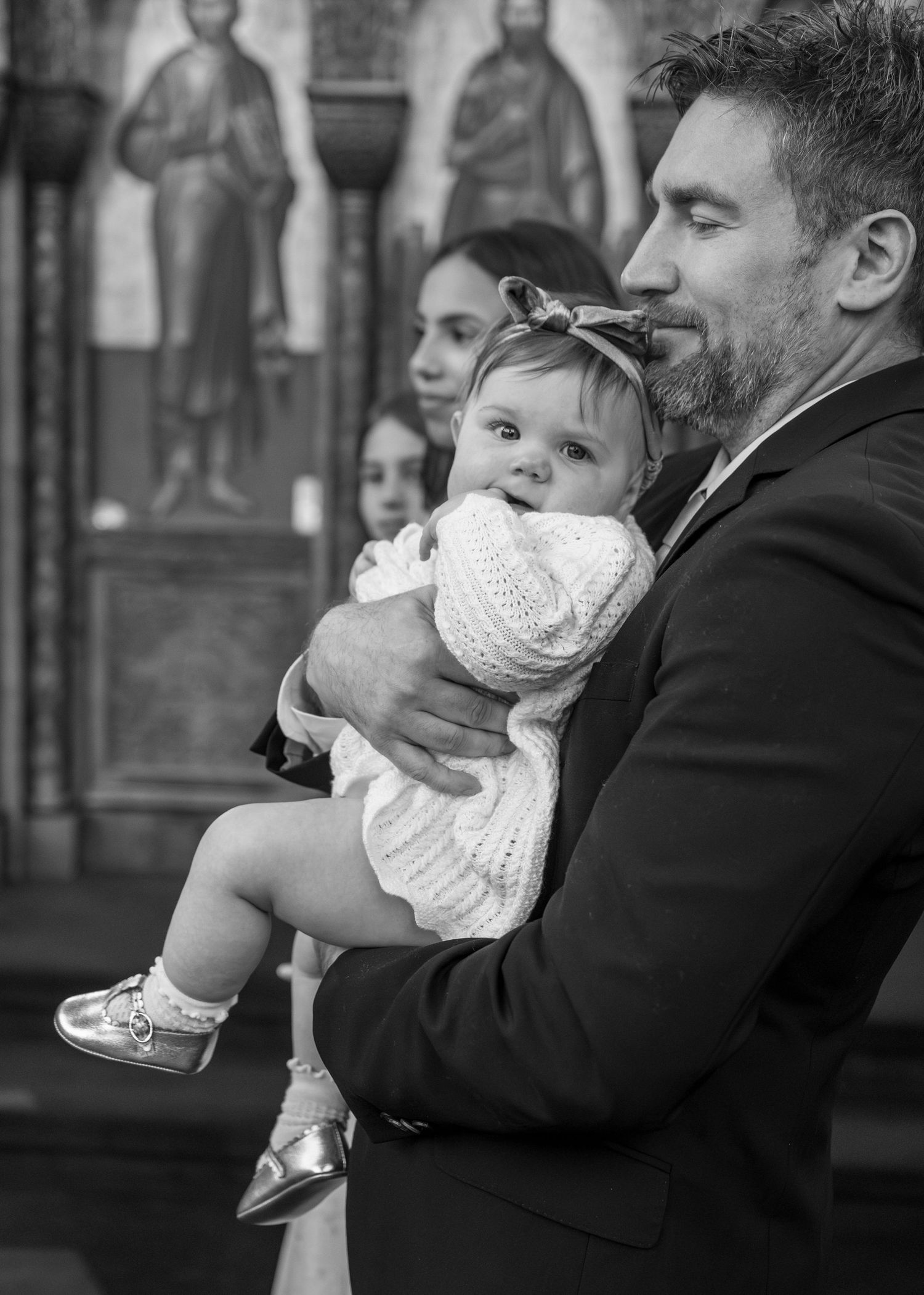 Man in suit holding a baby in white dress at a church baptism ceremony in black and white photo.