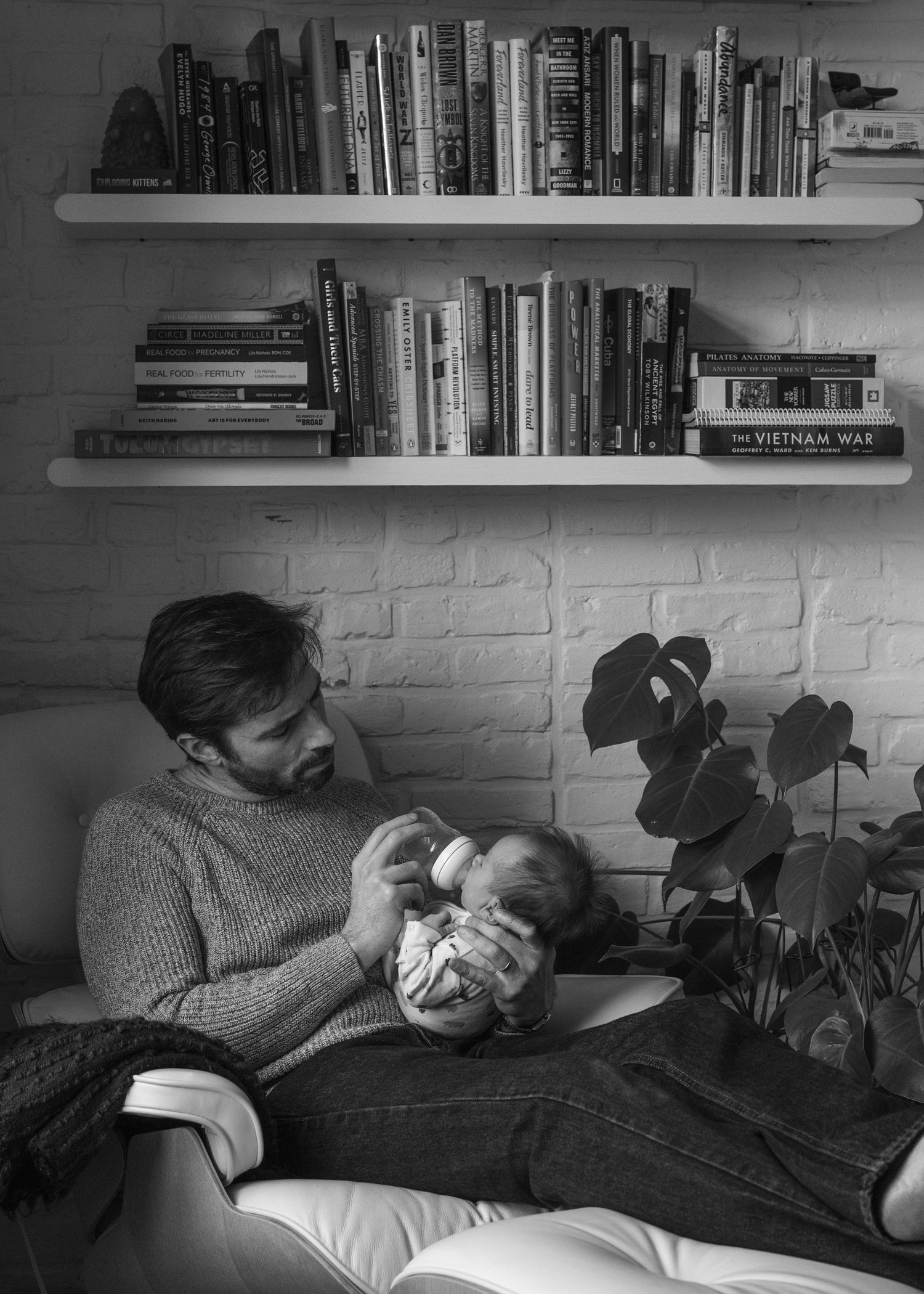 A cozy scene of parent feeding baby beneath bookshelves in a home setting.