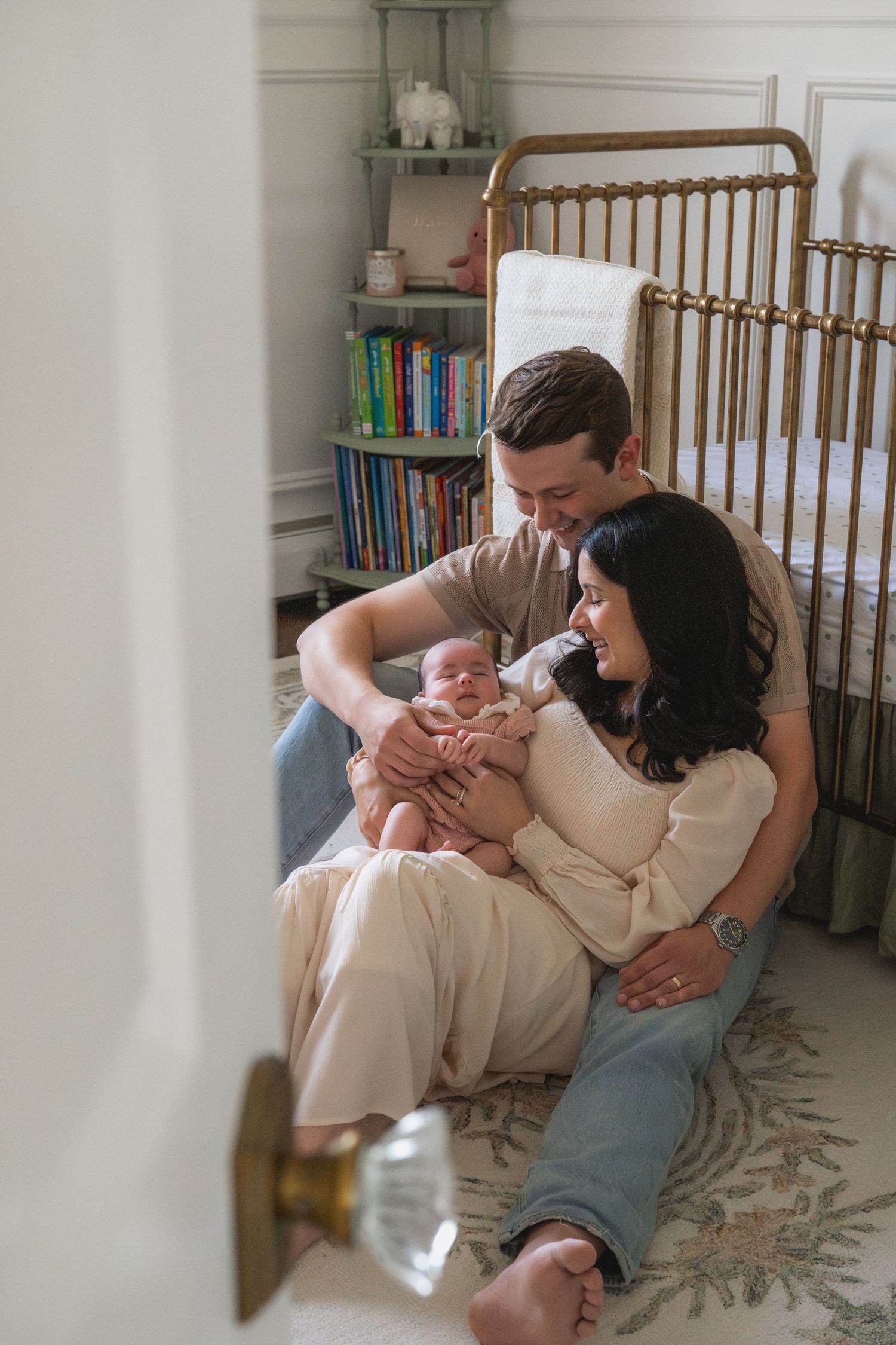 Family lounging together on floor cushions in a cozy nursery with wooden crib.
