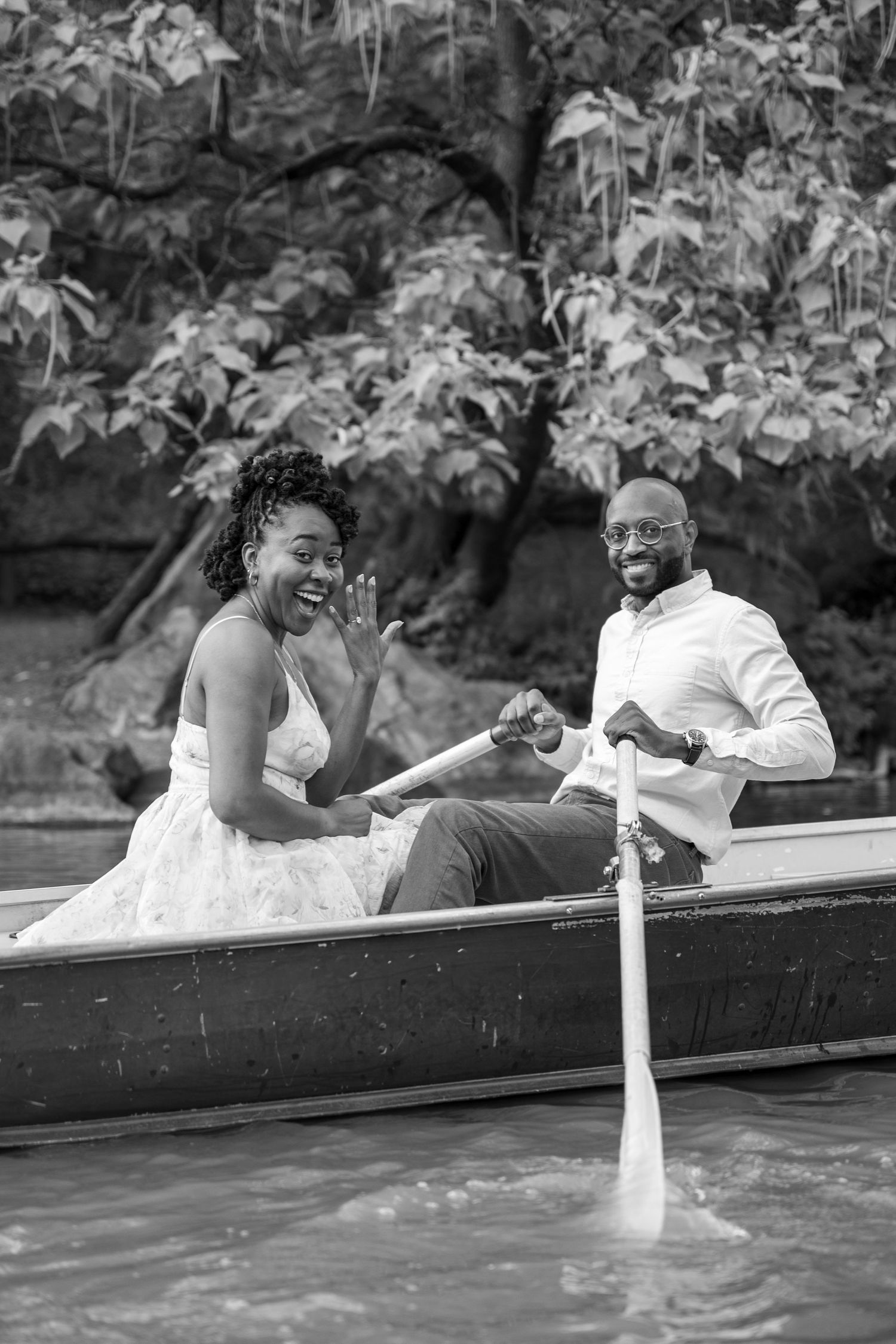 A couple shares a romantic moment while sitting in a boat on a lake in black and white.