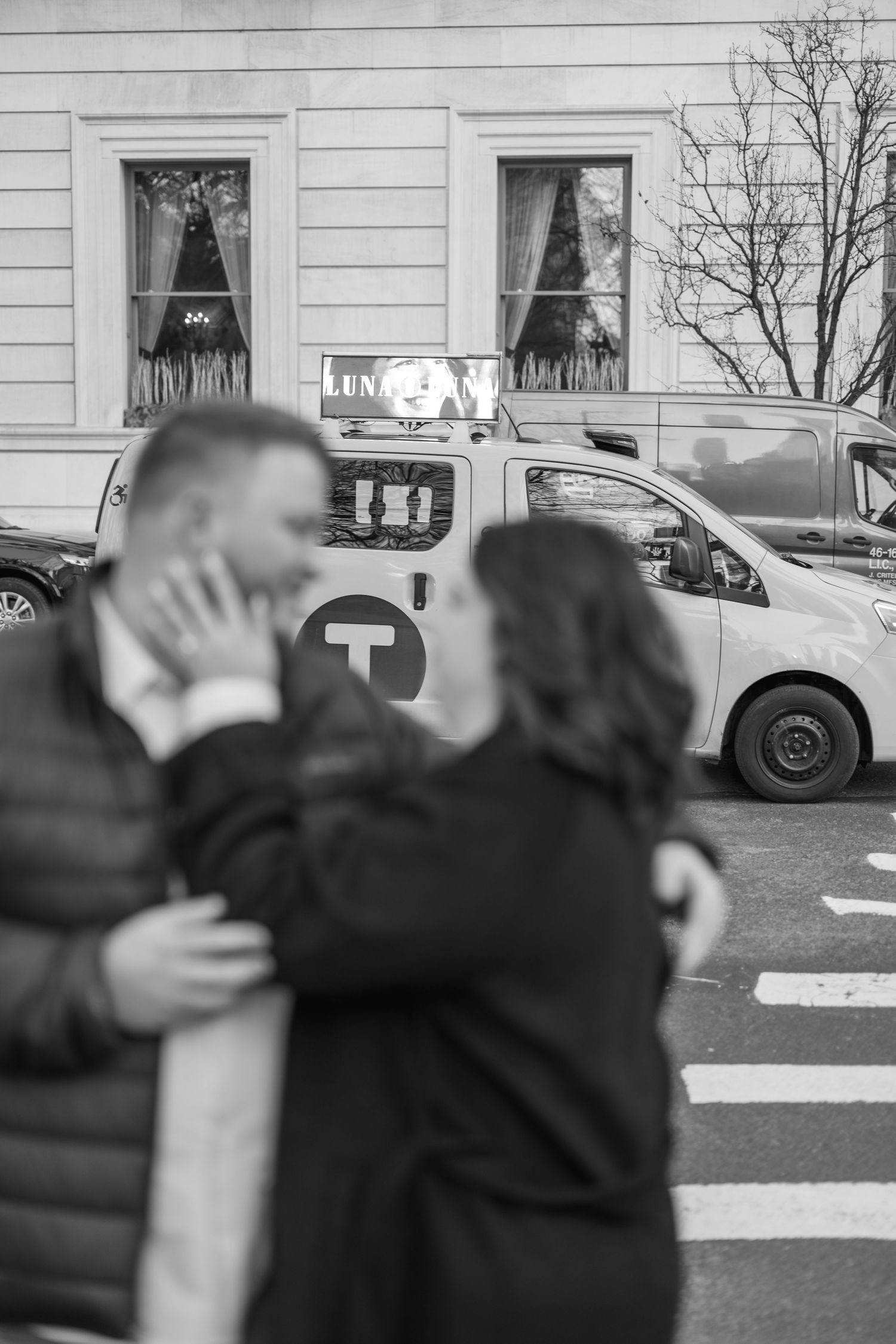A couple celebrates their engagement with an embrace in an urban parking lot setting.