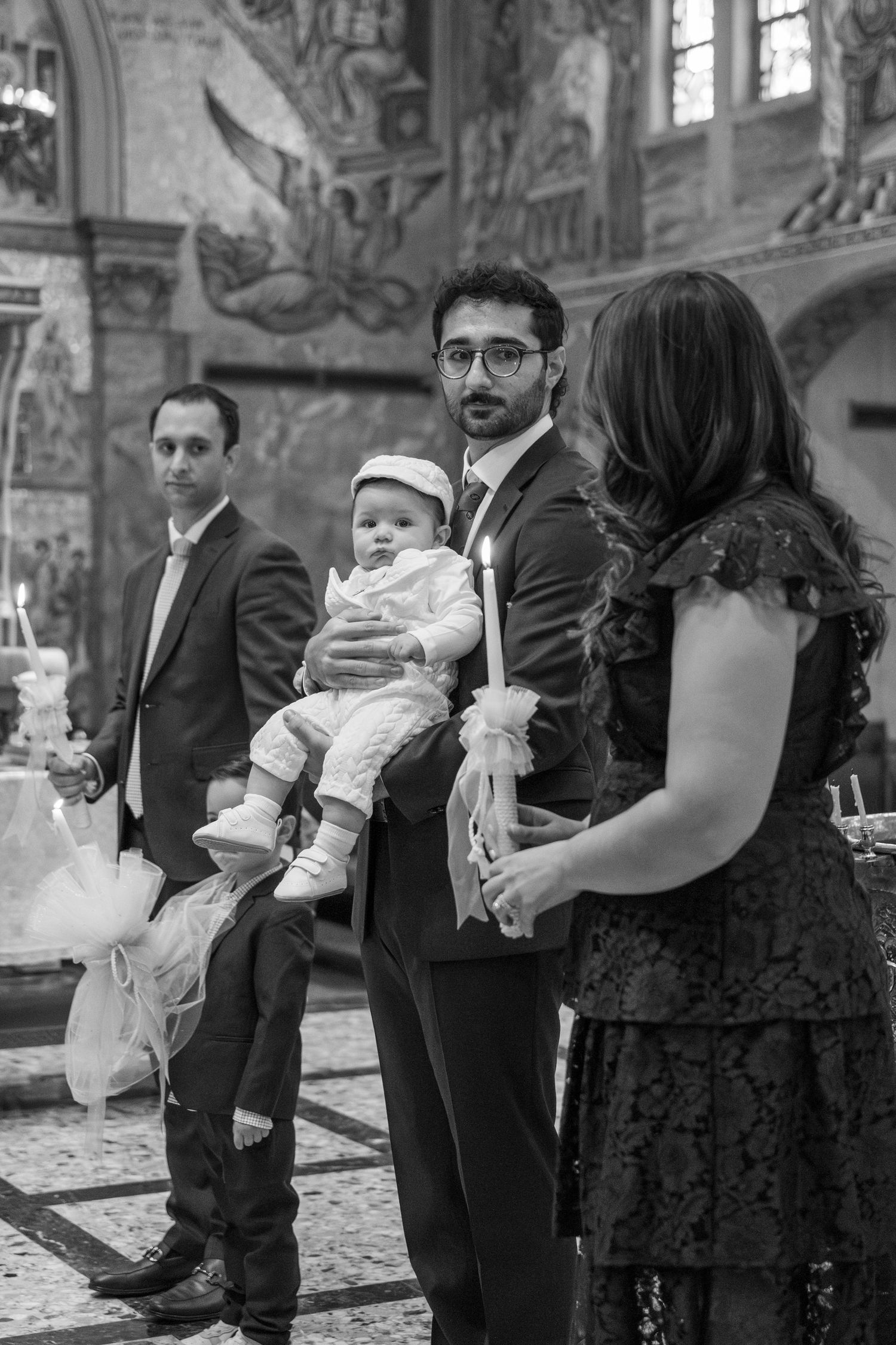 A formal baptism ceremony in a church with decorated walls featuring religious murals.