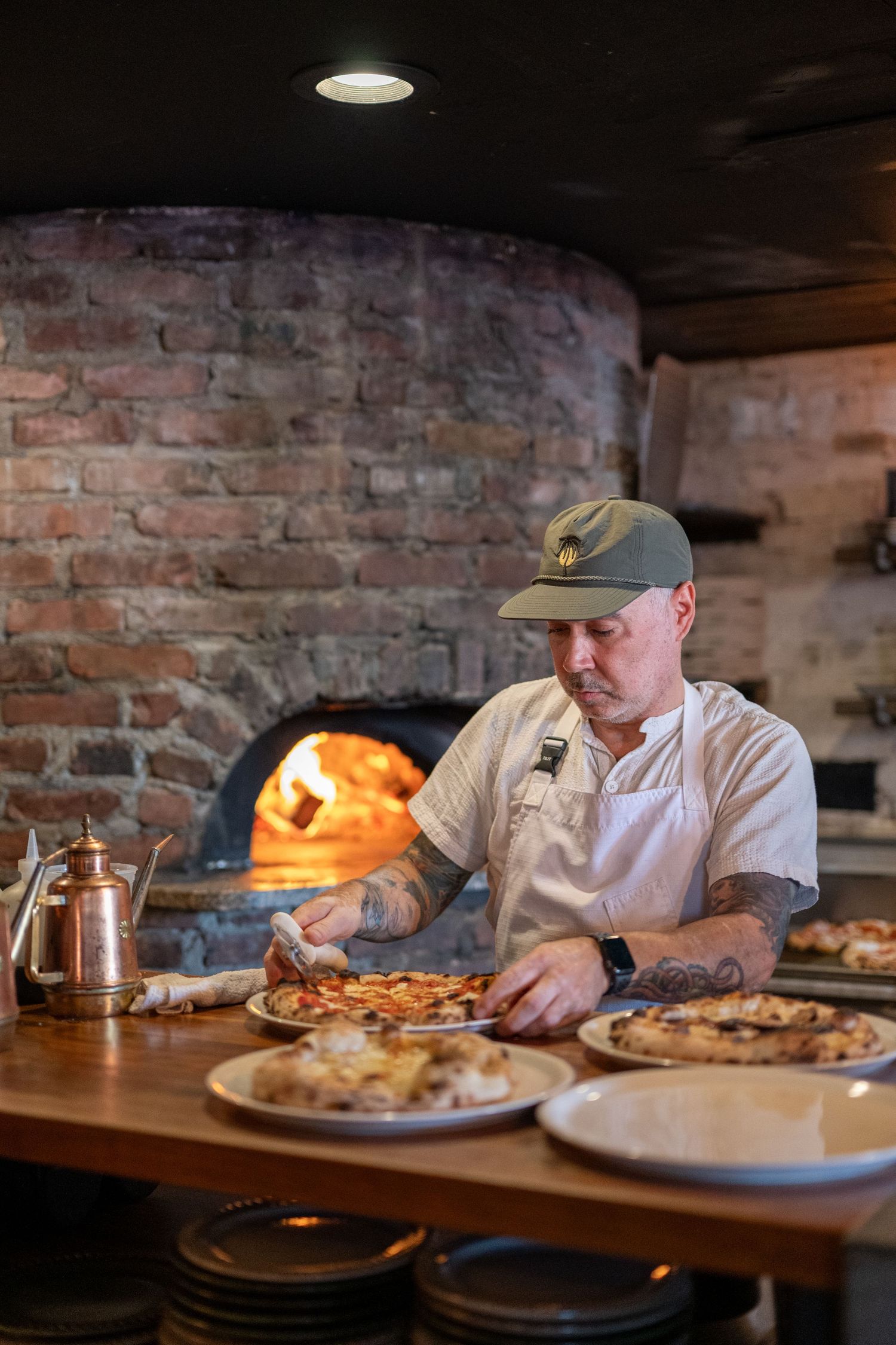 Chef working in a rustic restaurant with exposed brick walls and wood-fired oven in the background.