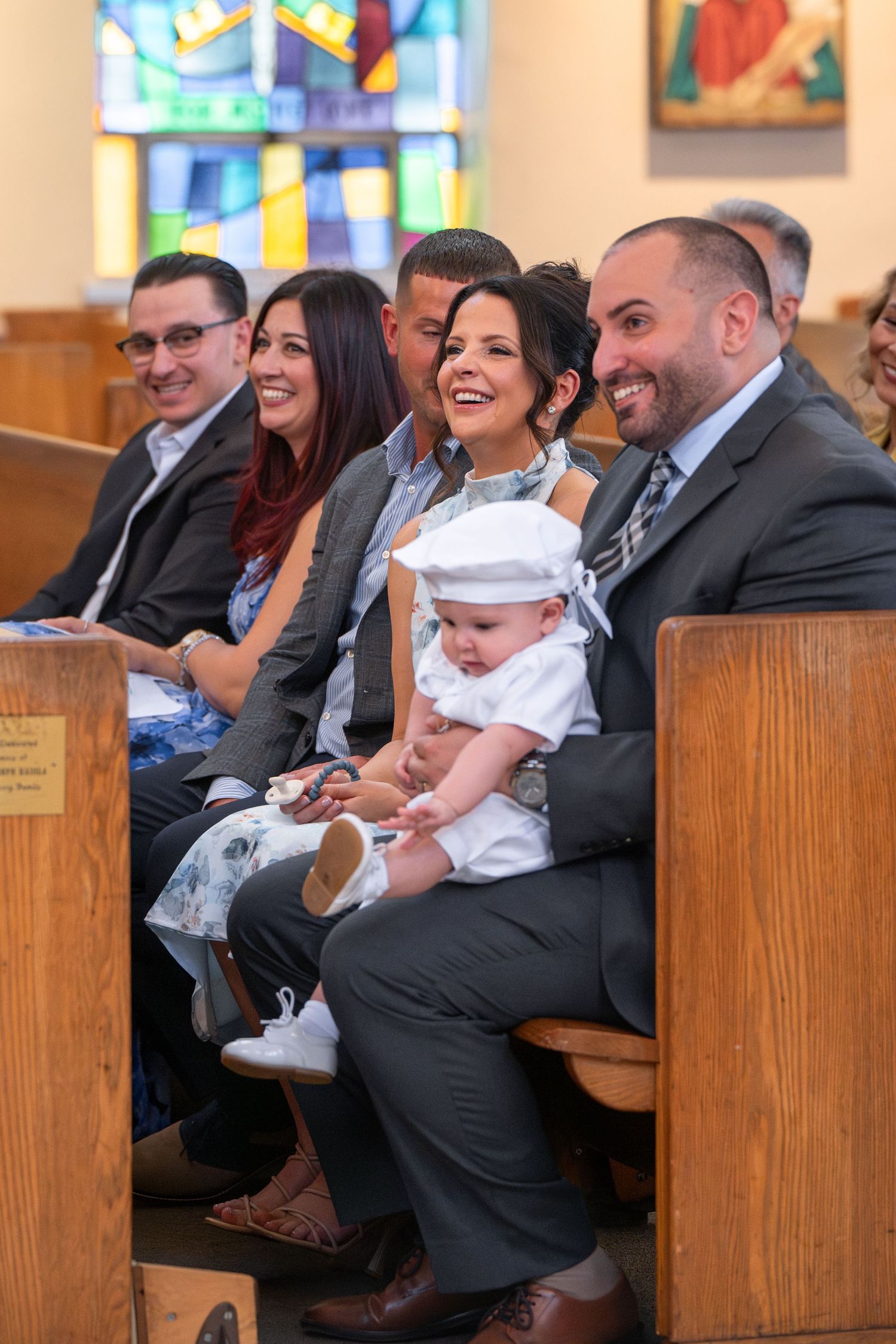 Multiple people seated in wooden church pews share joyful moments during a baptism ceremony.