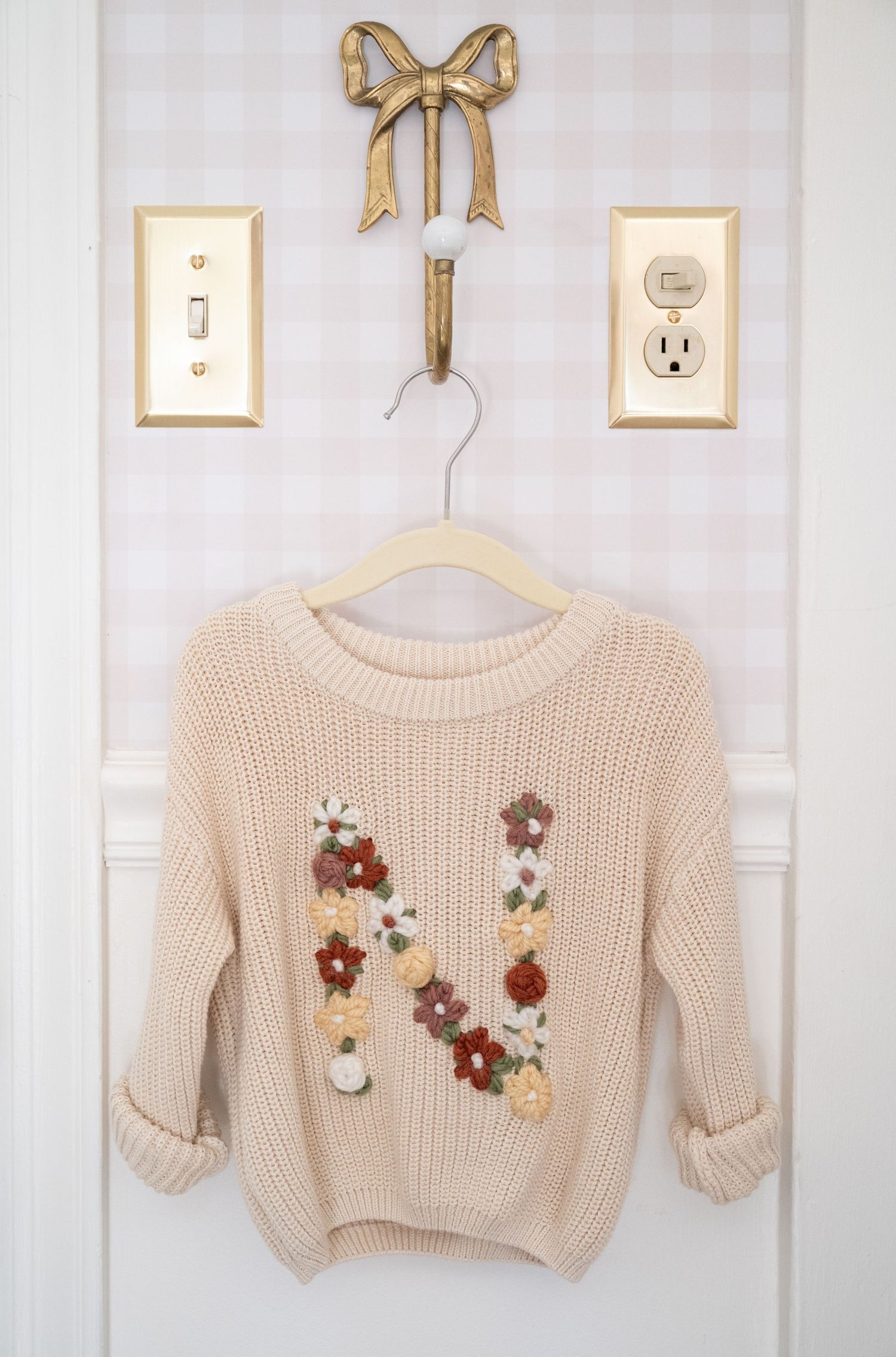 Cream colored knit sweater with floral embellishments hanging on display.
