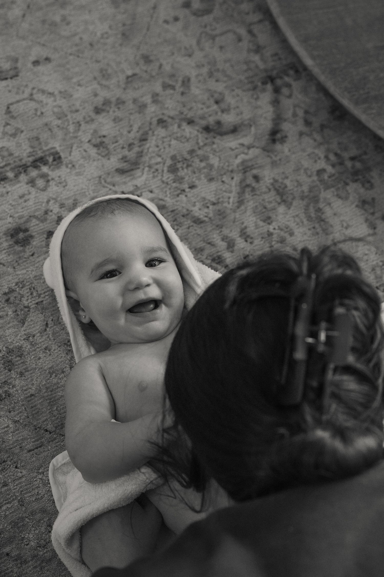 Black and white image of smiling baby wrapped in towel after bath time.
