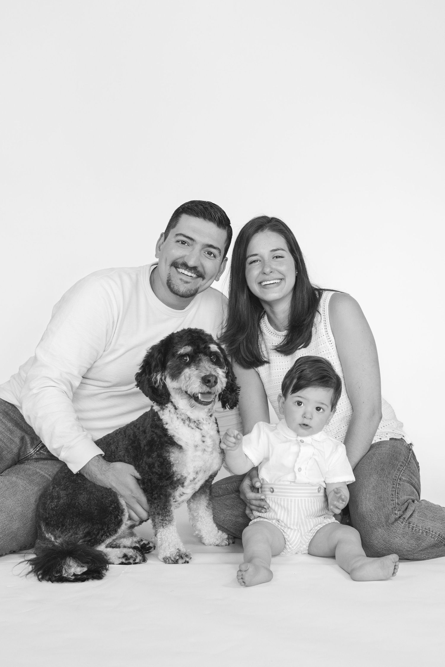 Studio portraits of a family with their black and white dog against white backdrop.