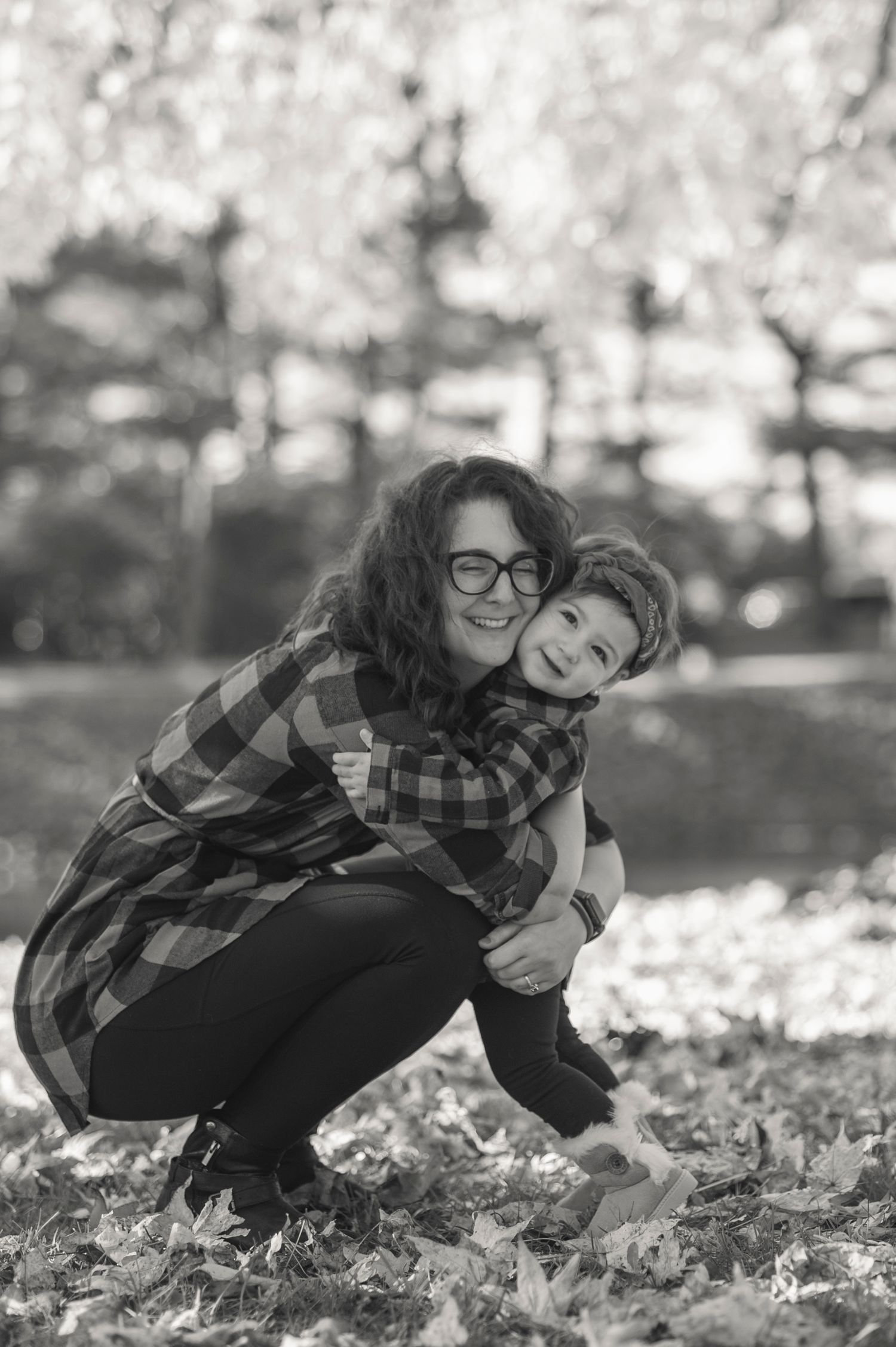 A black and white series shows two people playing together in autumn leaves on the ground.