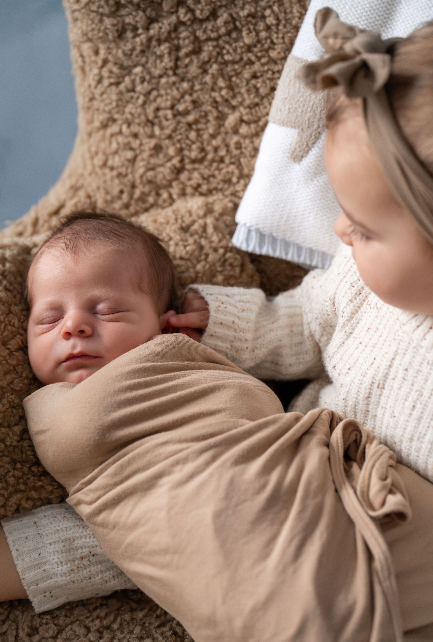 A sleeping newborn baby swaddled in a beige blanket rests peacefully on a brown textured surface.