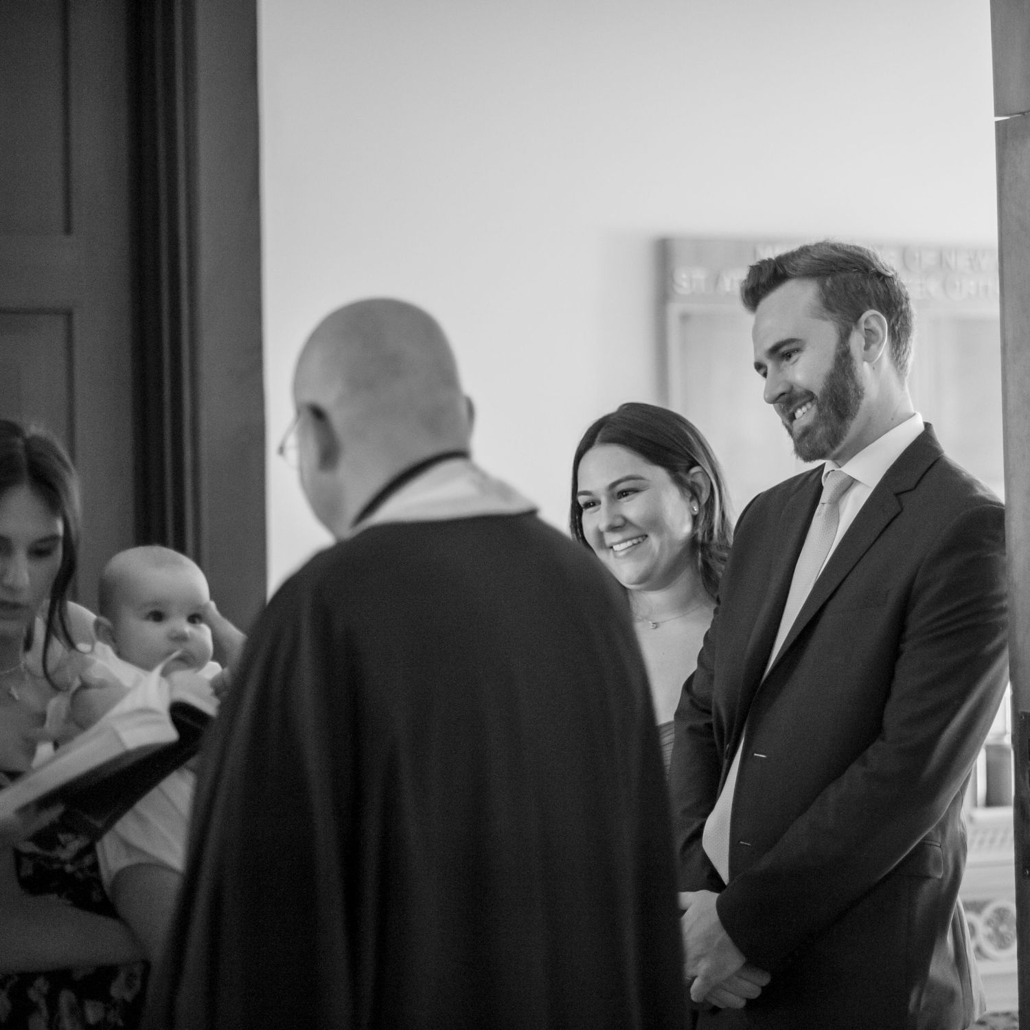 A black and white photograph of a baptism ceremony with people gathered around a baby at the church.