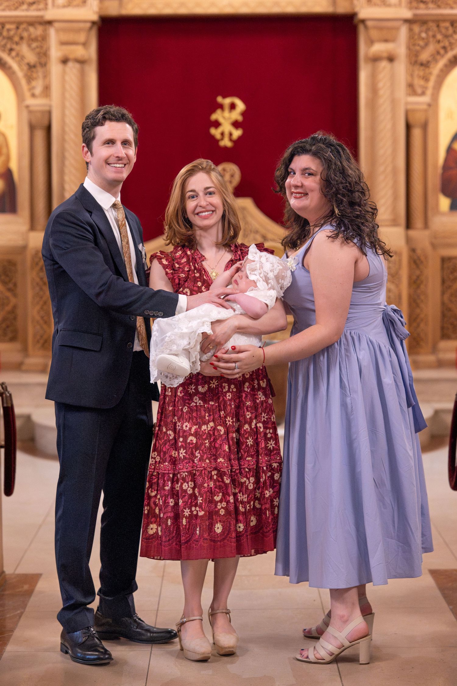 A baptism ceremony takes place in an elegant church with red and gold decor.
