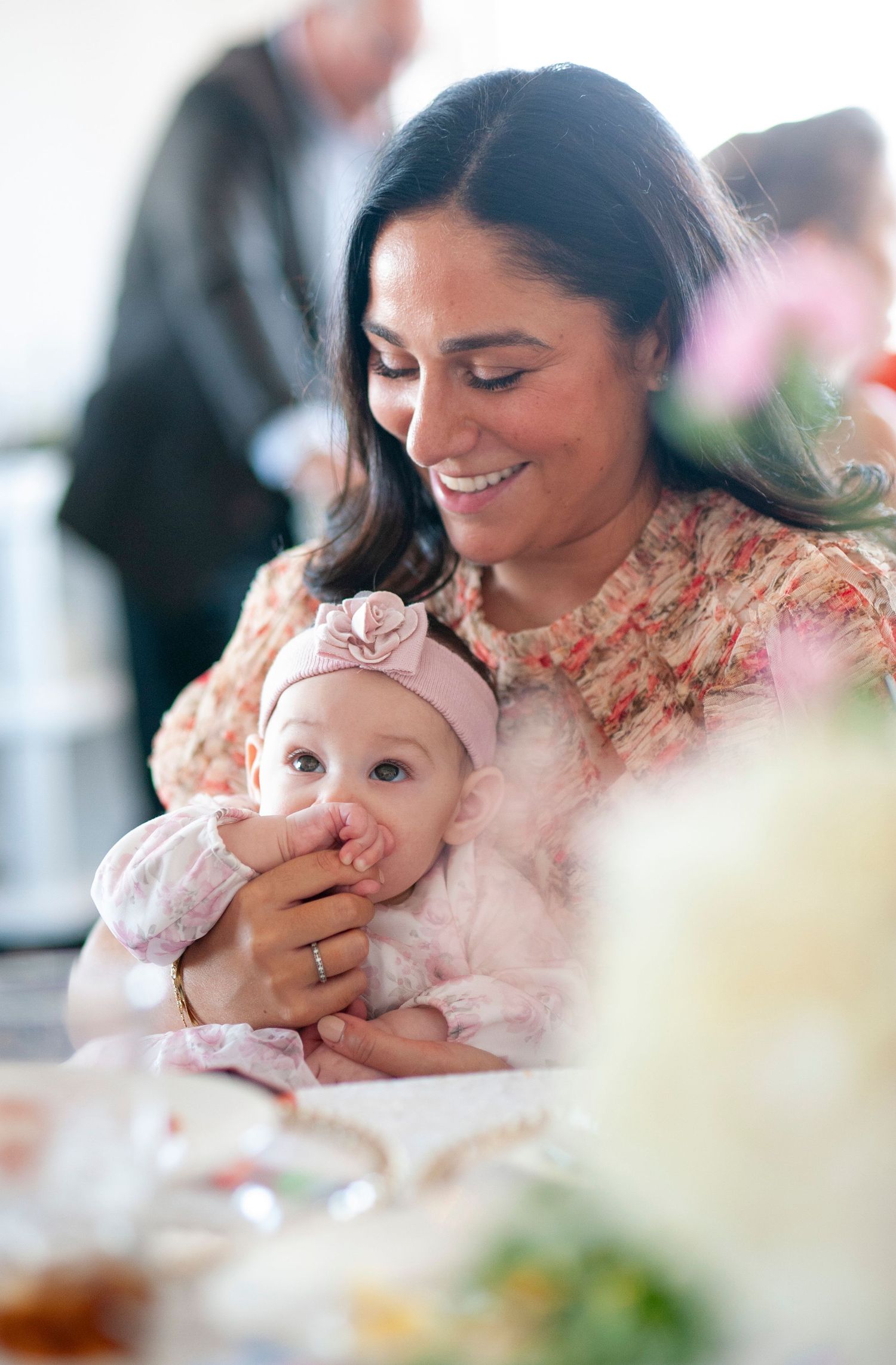 Mother and baby sharing tender moment at celebration event with floral decor.