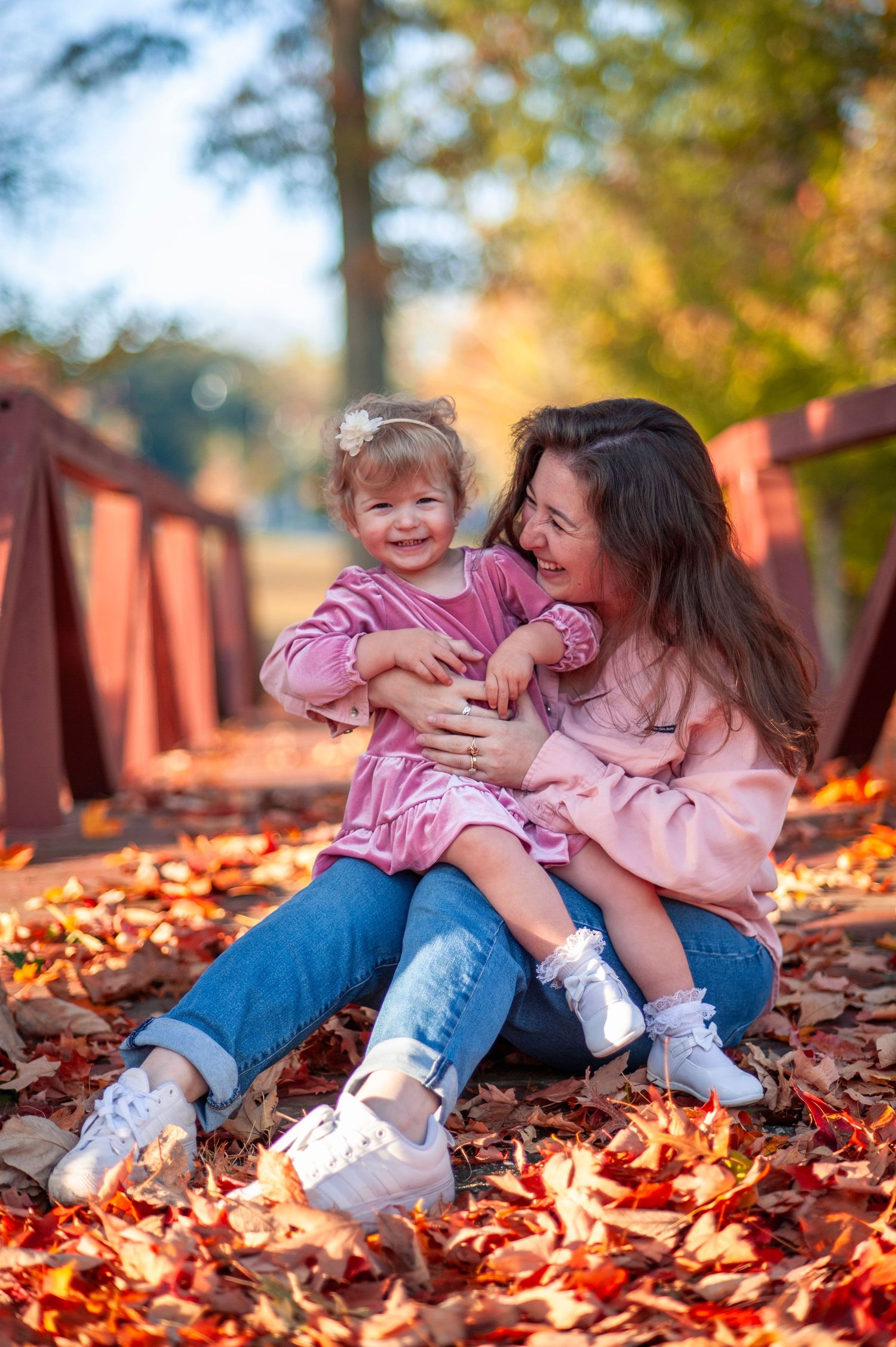 Mother and child playing in autumn leaves wearing matching pink outfits.