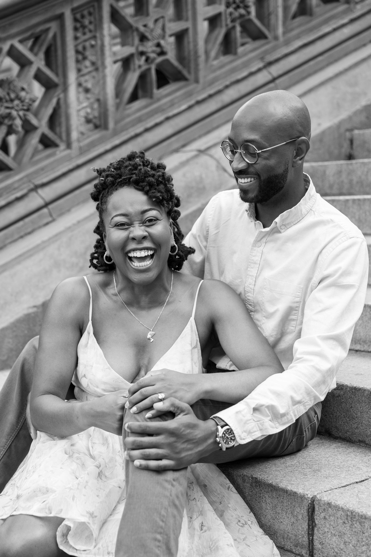 Joyful couple sharing genuine laughter while sitting on stone steps outdoors.