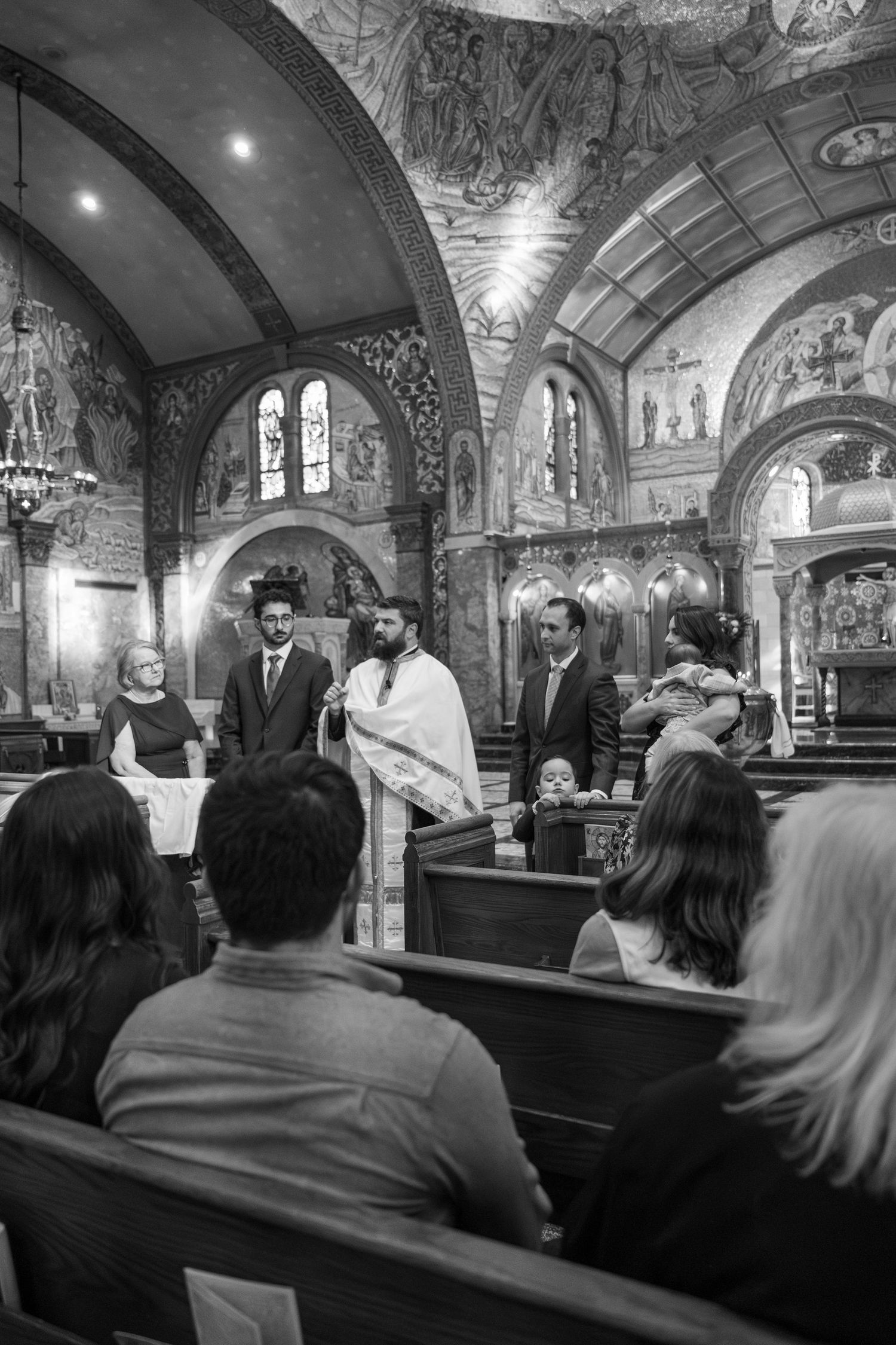 Black and white photograph of baptism ceremony in historic church with decorated walls.