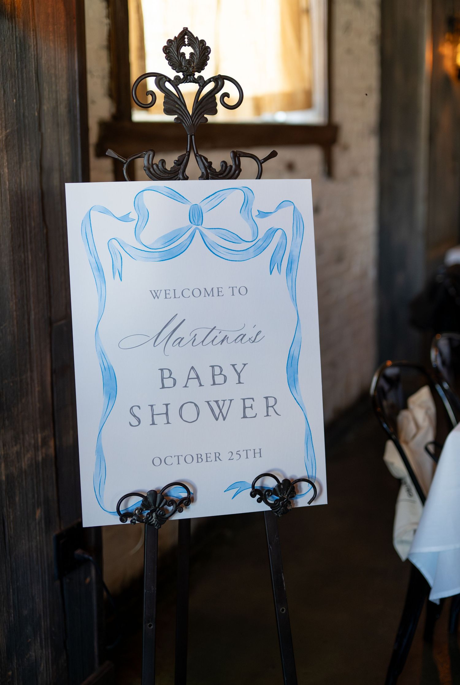 Elegant baby shower welcome signs with blue decorative details mounted on ornate black metal stands.