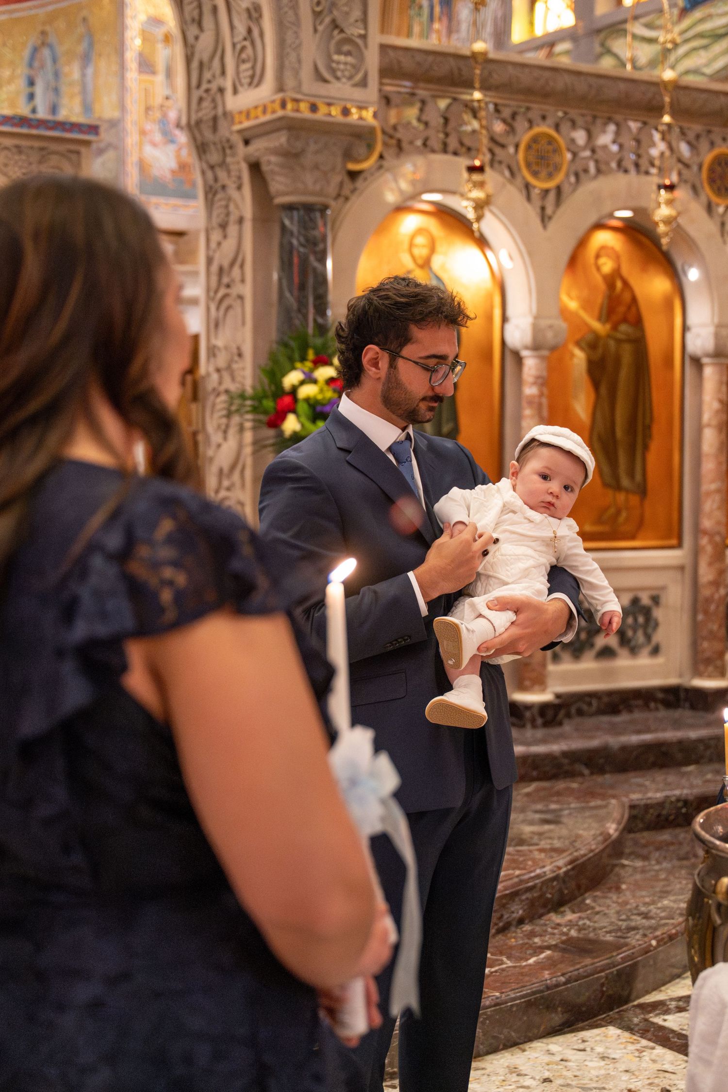 Baptism ceremony taking place in beautifully decorated Orthodox church interior.