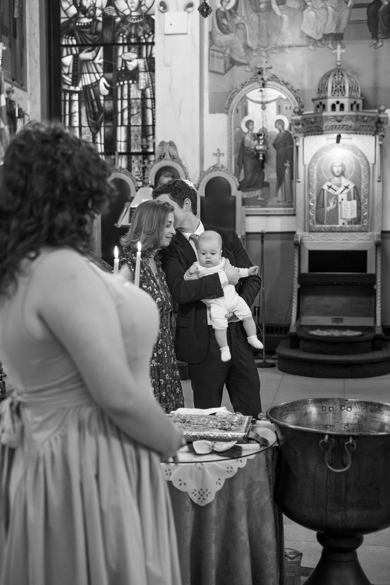 A baptismal ceremony taking place at a traditional church font with attendees gathered around.