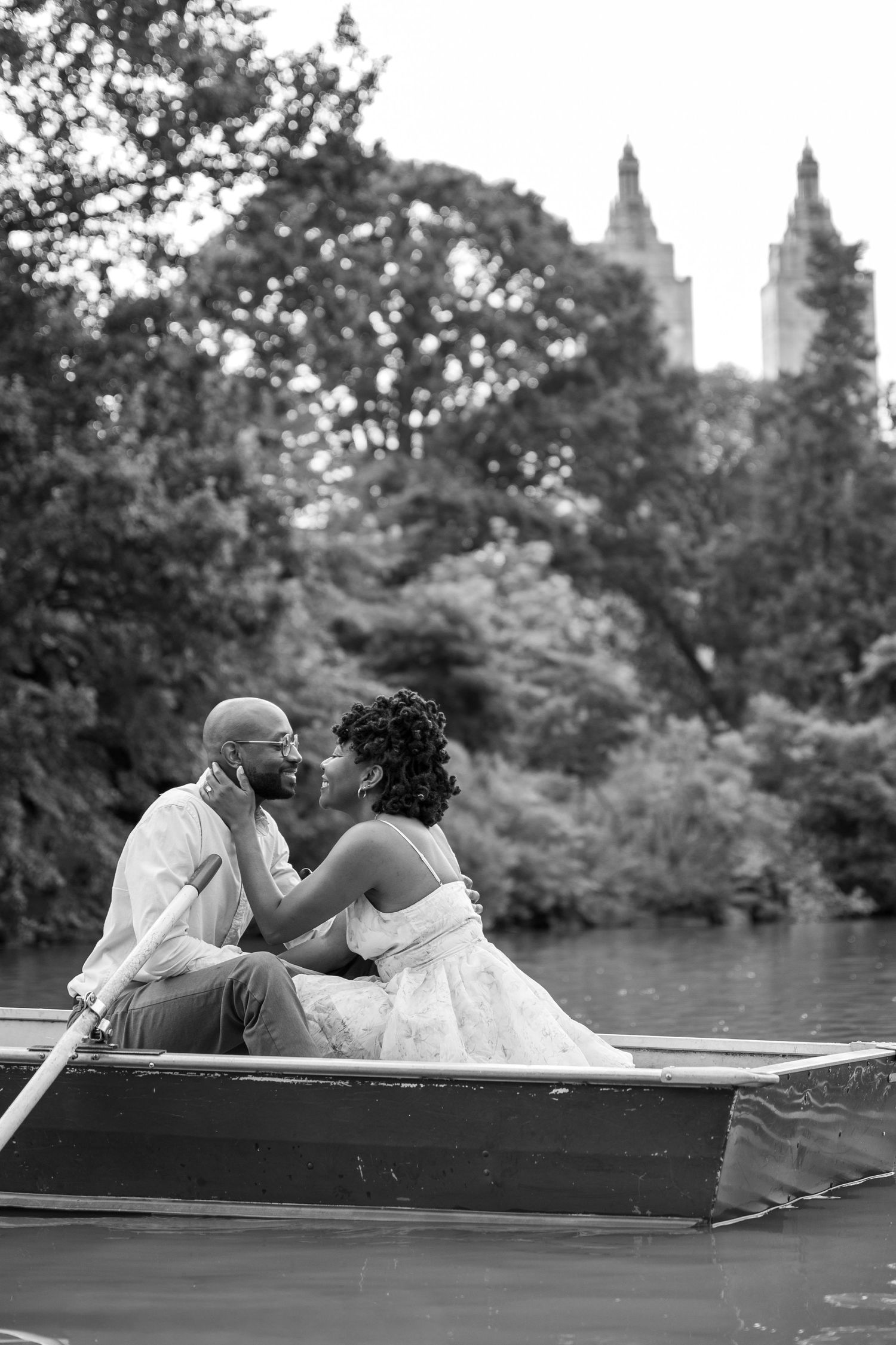 A couple sharing intimate moments while sitting in a rowboat on a lake in Central Park in black and white photos.