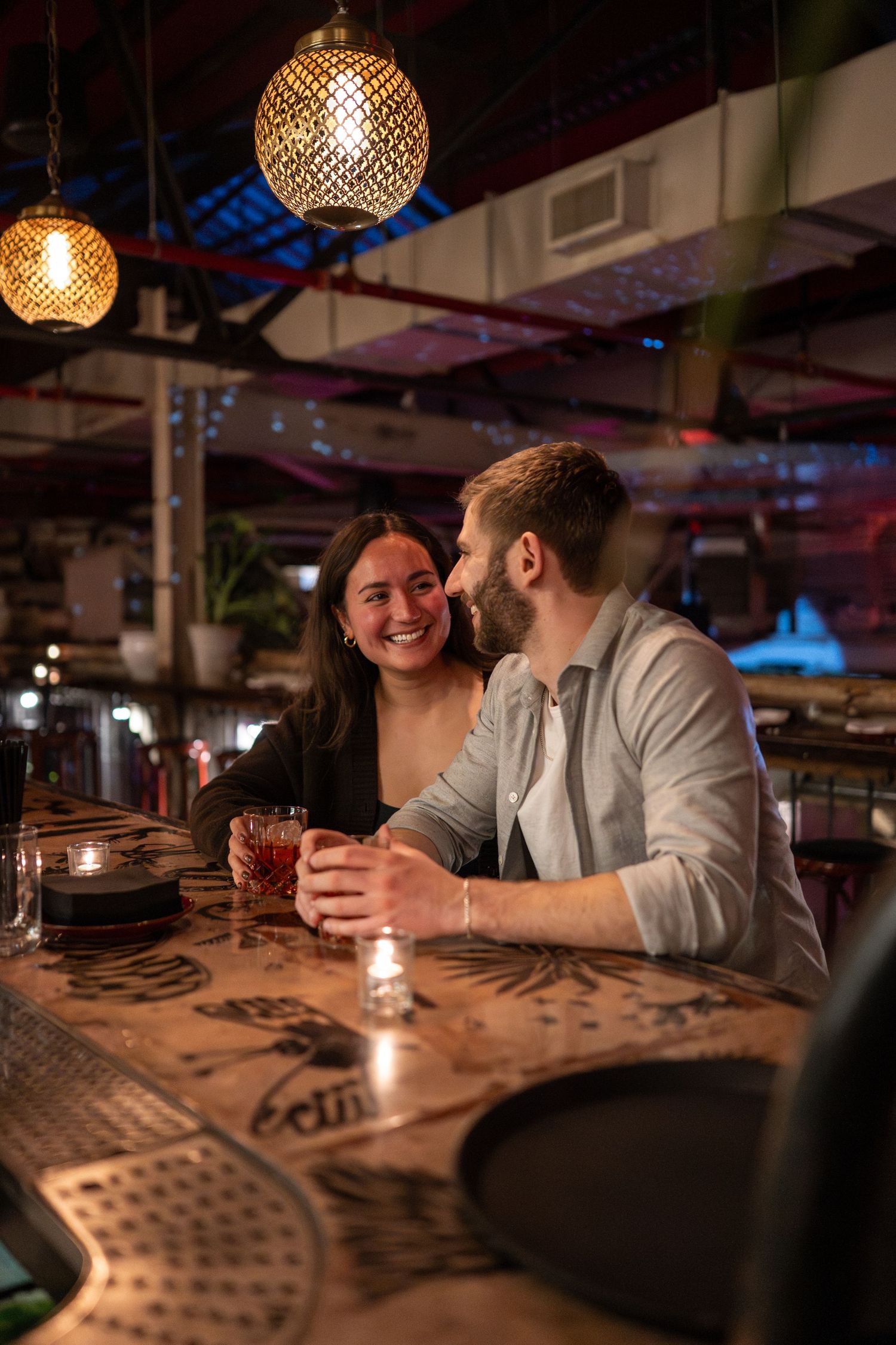 A couple enjoying drinks together at a dimly lit bar with decorative pendant lighting.