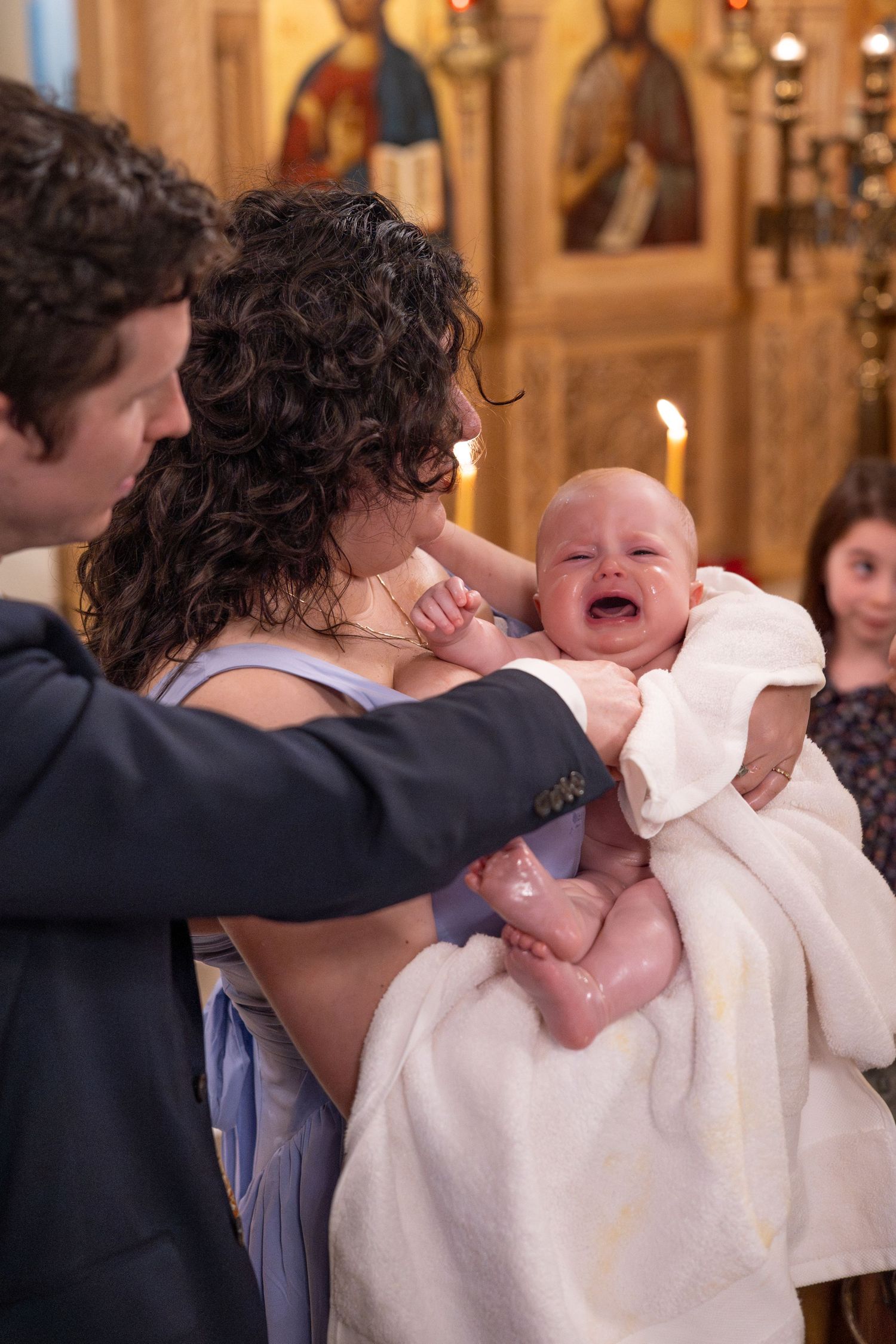 An emotional moment during a baptism ceremony as a baby is held in white clothing.