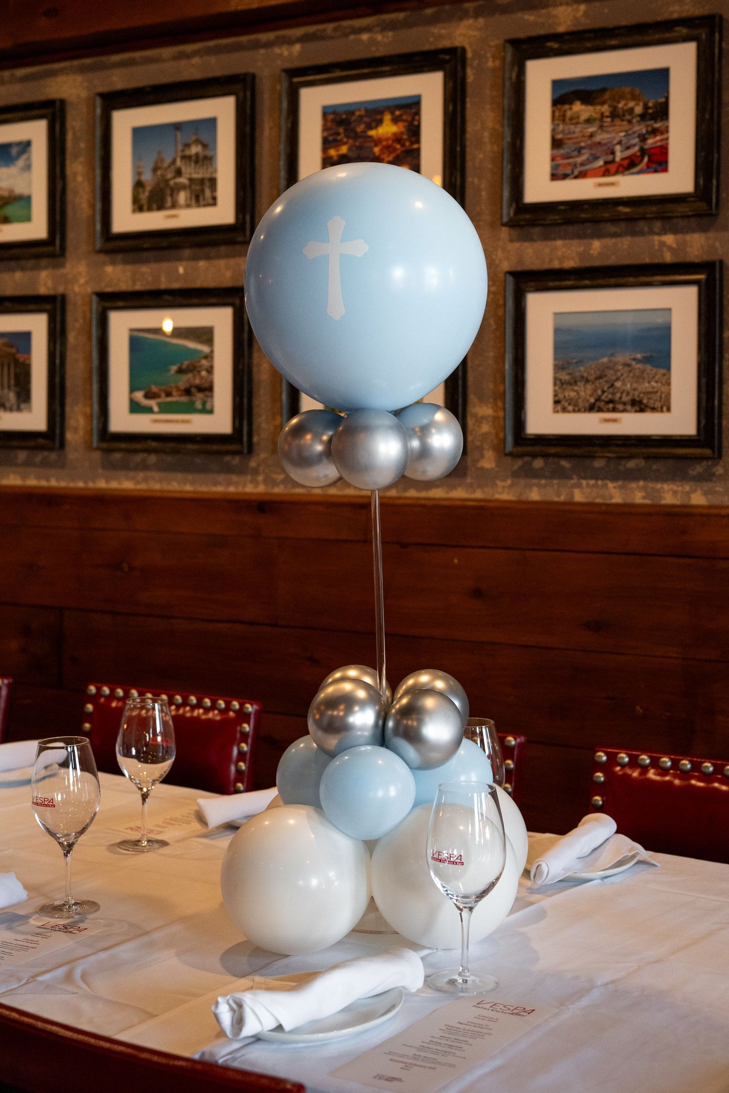 Light blue and silver balloon centerpiece with cross design on dining table with wine glasses.