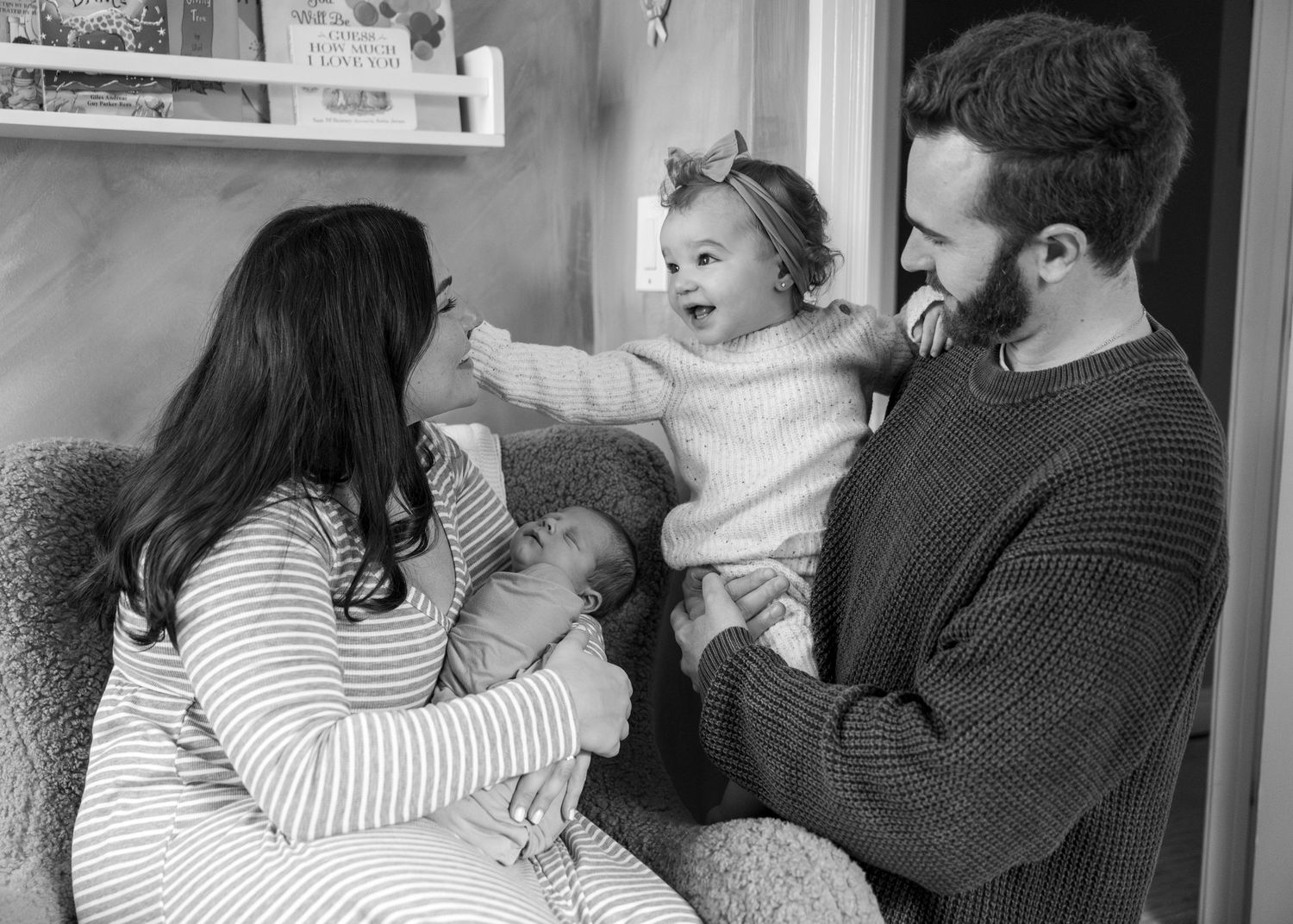 A family shares a tender moment together in black and white, sitting close on a couch in their home.
