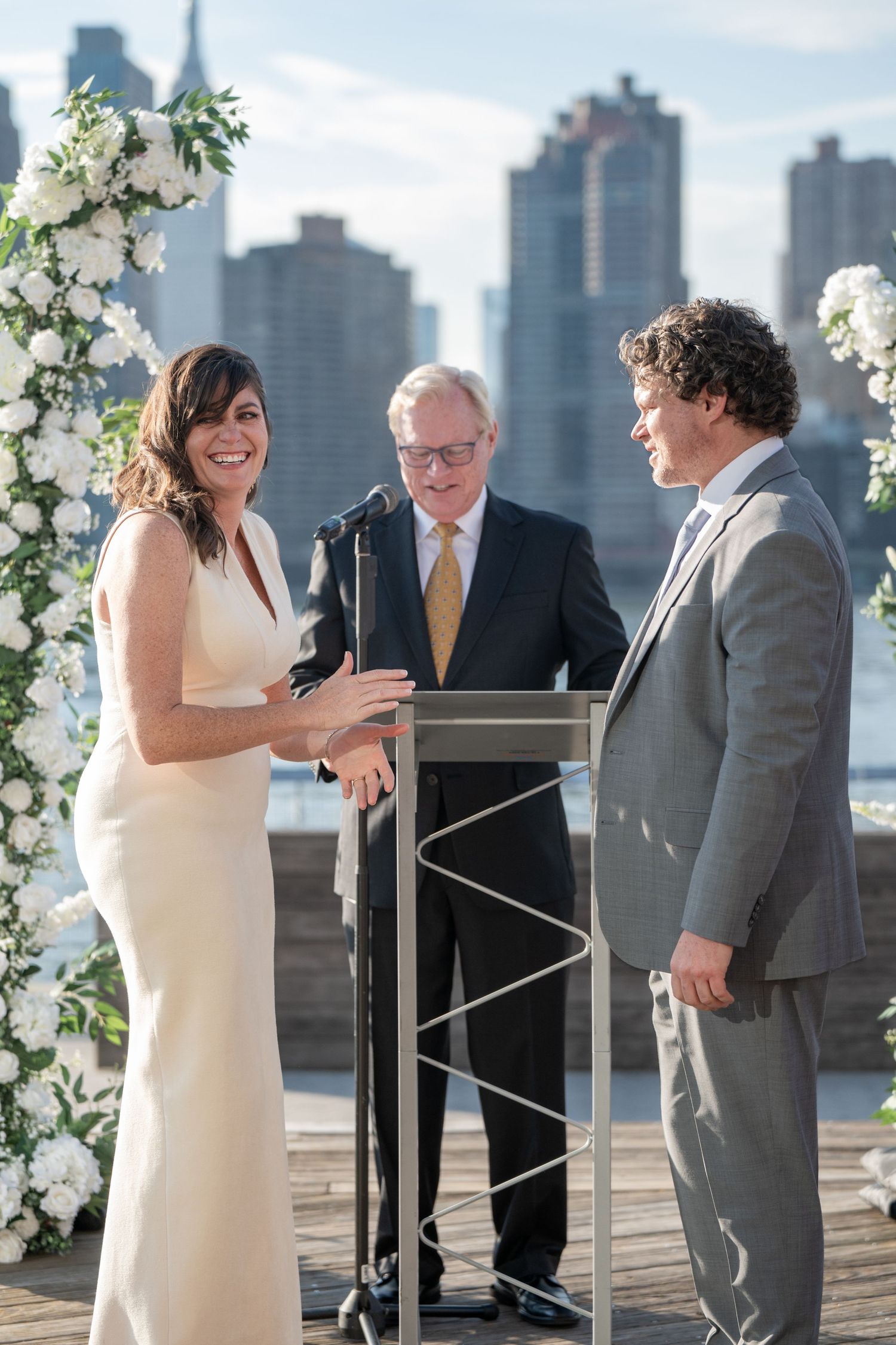 Wedding ceremony participants share joyful moments on an outdoor deck with city skyline in background.