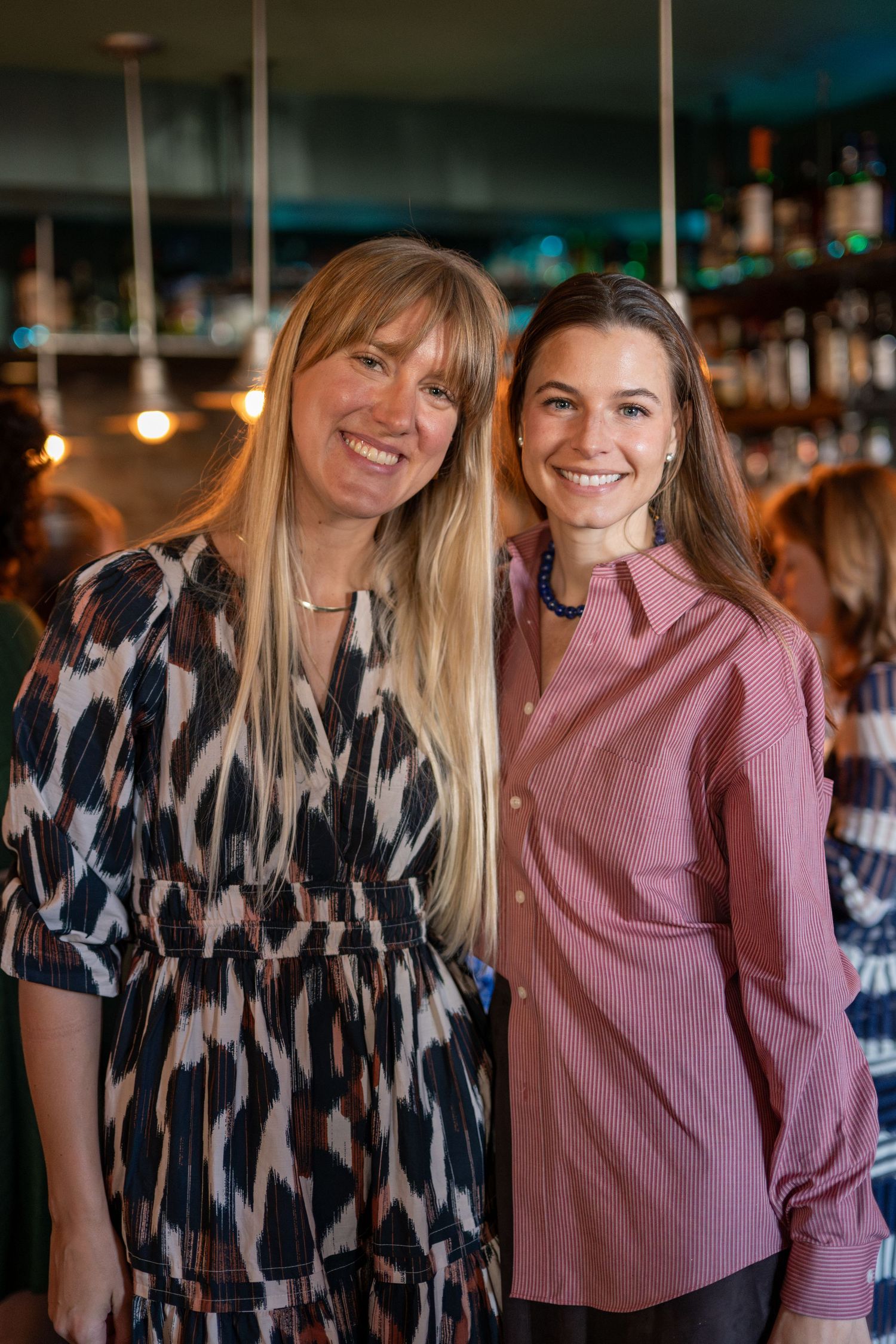 Friends in patterned dresses smiling and laughing together at a social event.