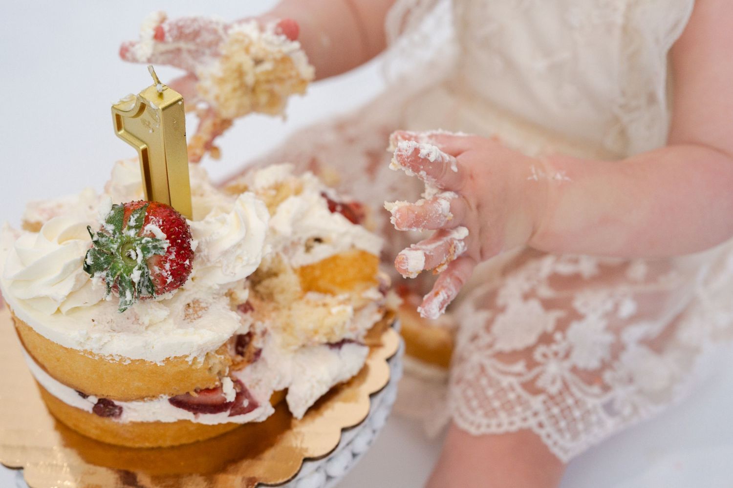 A messy cake smash photo session showing small hands reaching for frosting and cake decorations.