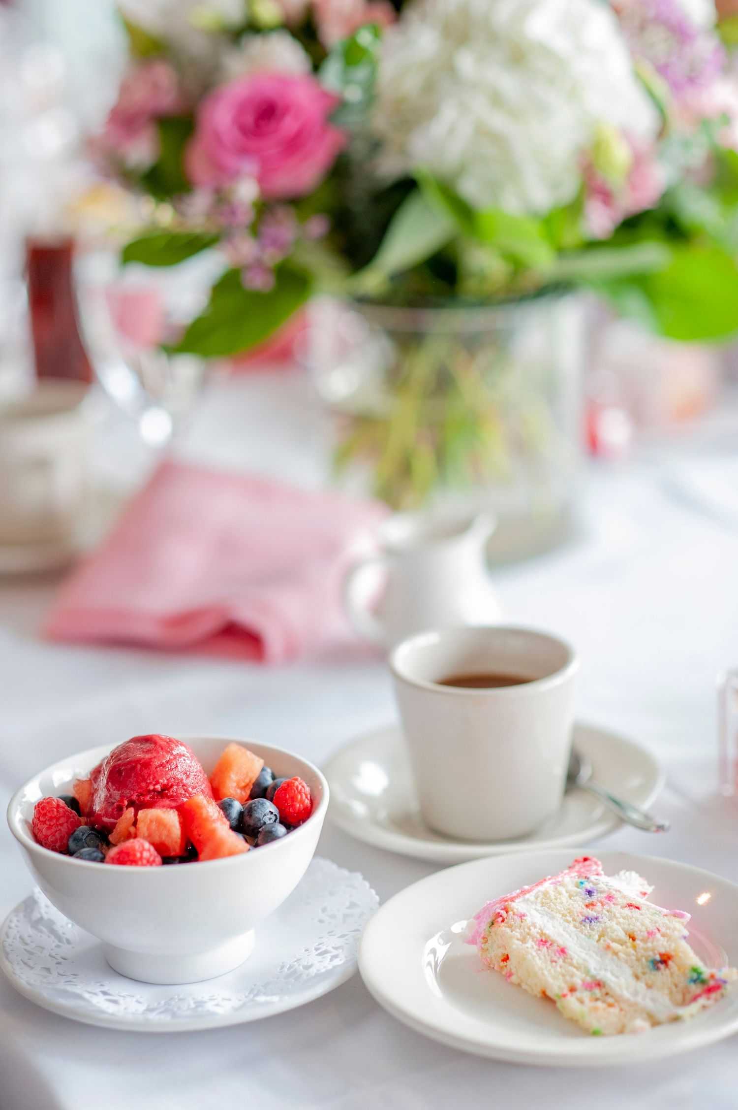 Elegant table setting with fresh flowers, berries, and tea cups in soft pink and white tones.