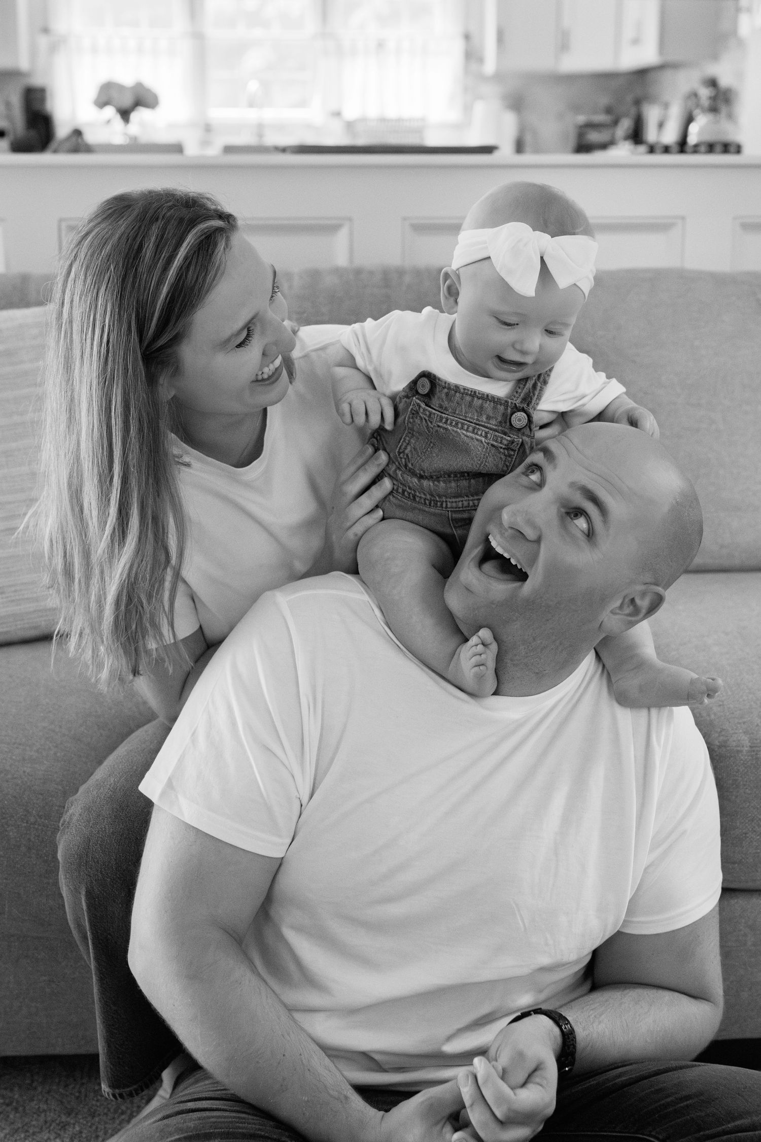 Candid black and white photos show playful moments of laughter and joy between family members on a couch.