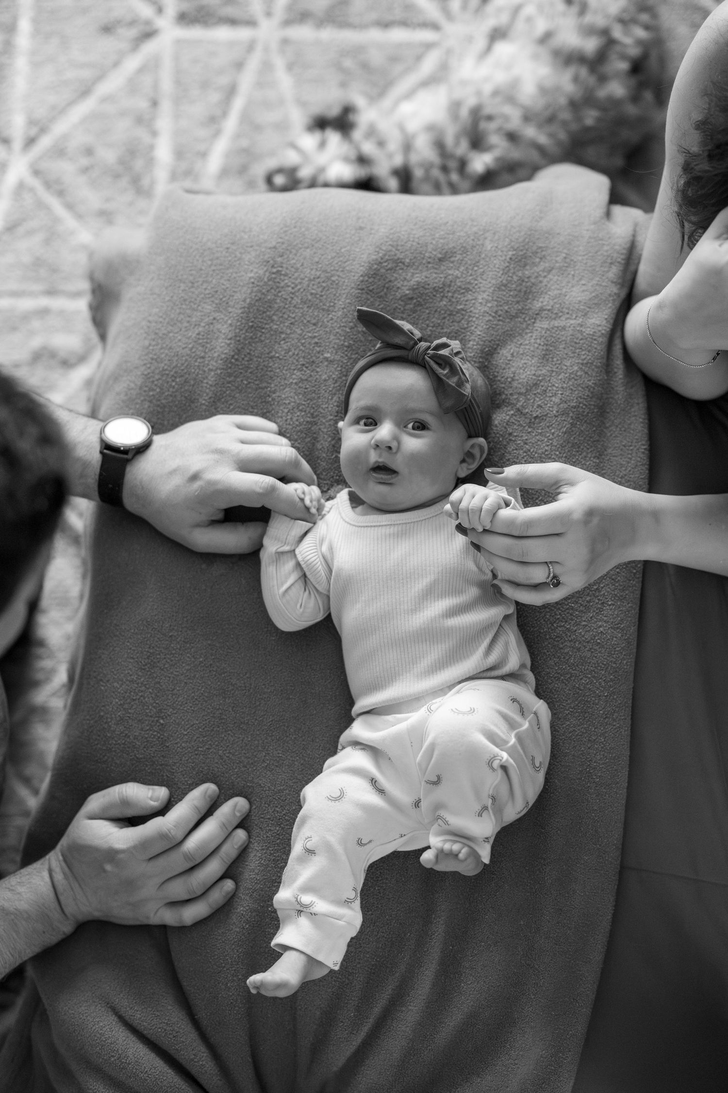 Black and white photo series showing a baby lying on couch while hands adjust their position.