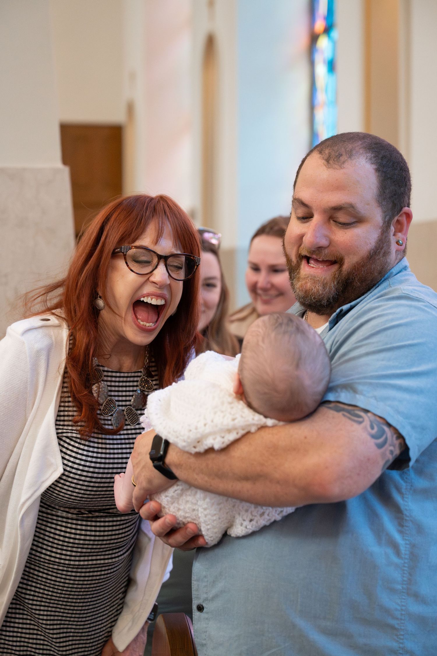 A group shares a joyful moment while holding a baby in a church setting.