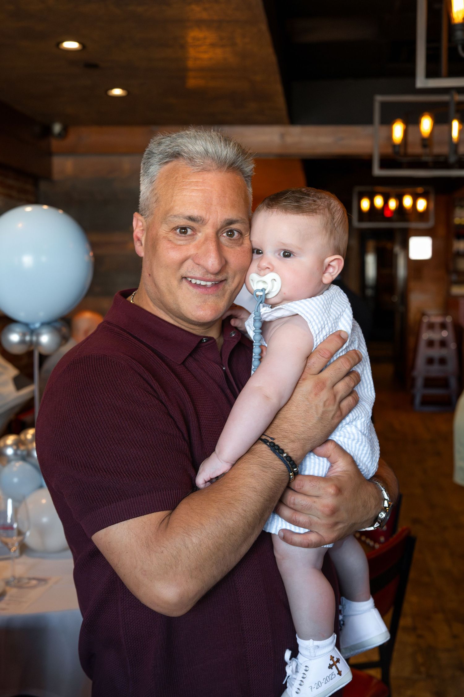 A celebration event in a restaurant with festive blue balloons and a baby in white clothing.