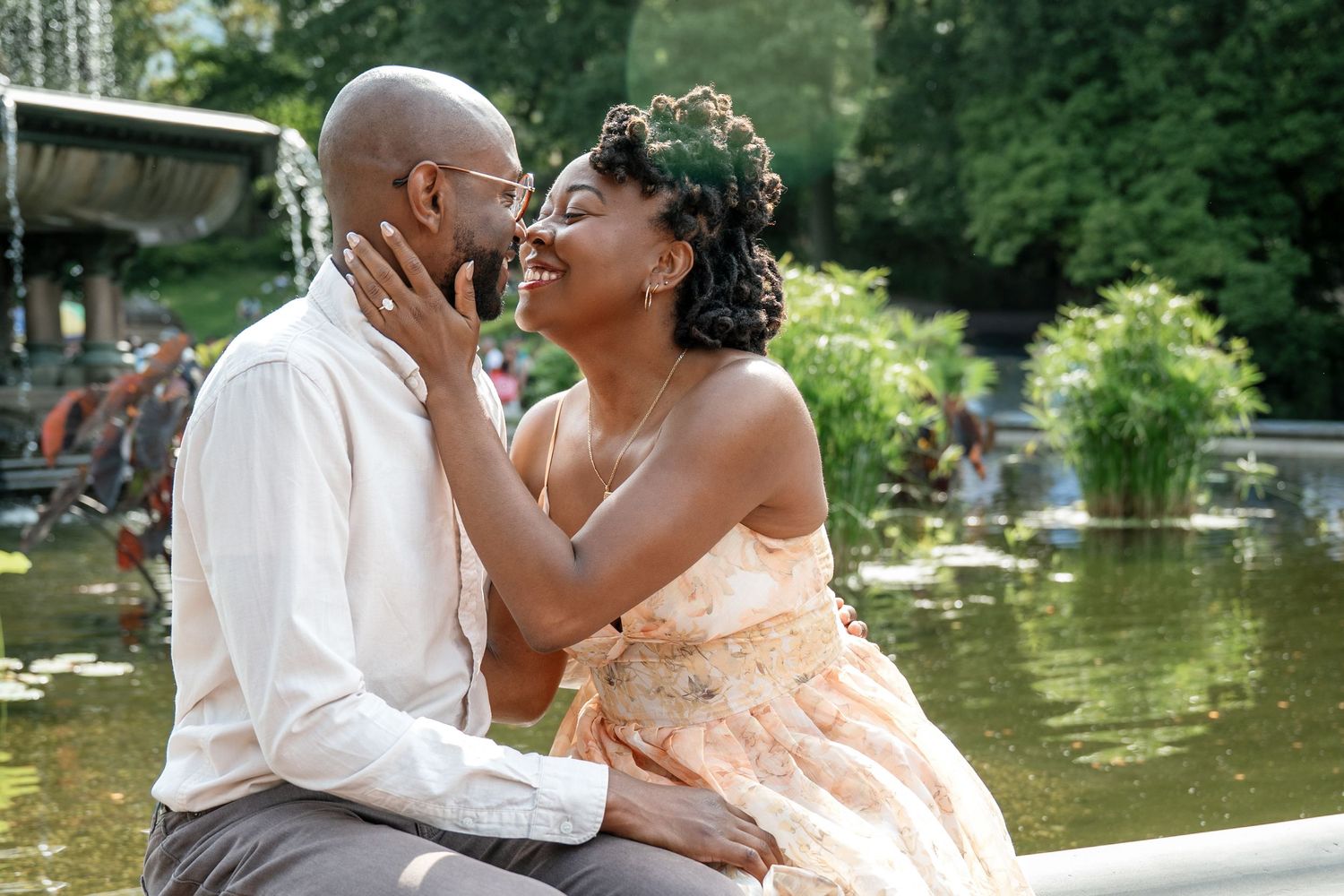 A romantic couple in formal attire shares tender moments by a serene lake in a garden setting.