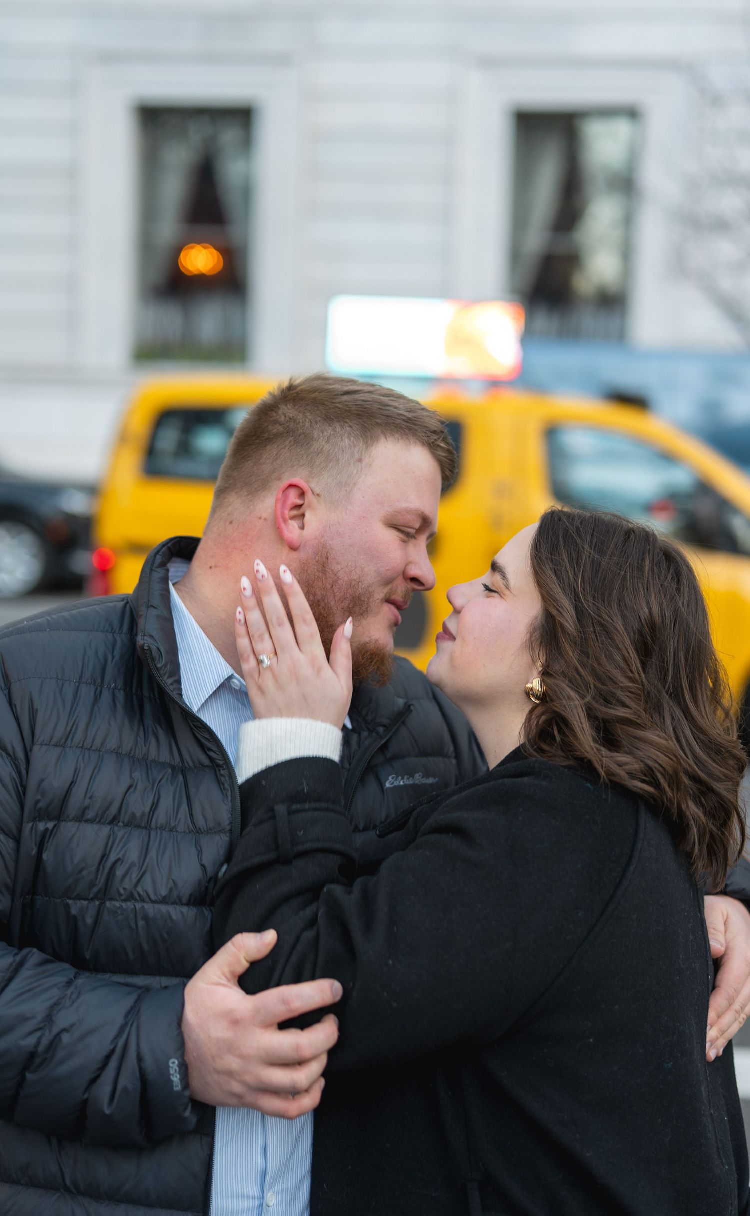 Couple sharing an intimate moment in front of yellow taxis in an urban setting.