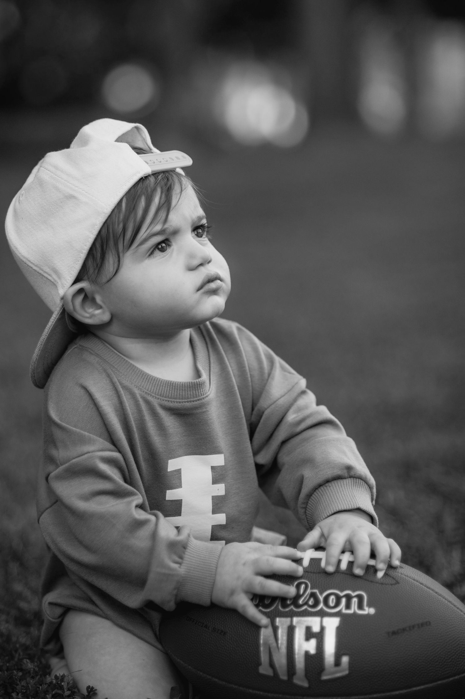 Black and white photos of a baby in a cap with NFL football equipment.