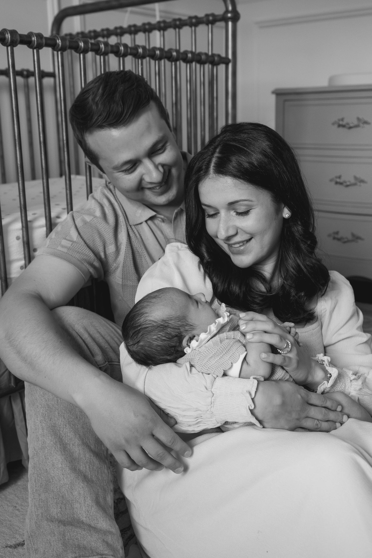 Black and white series of tender family moments near an iron bed frame.