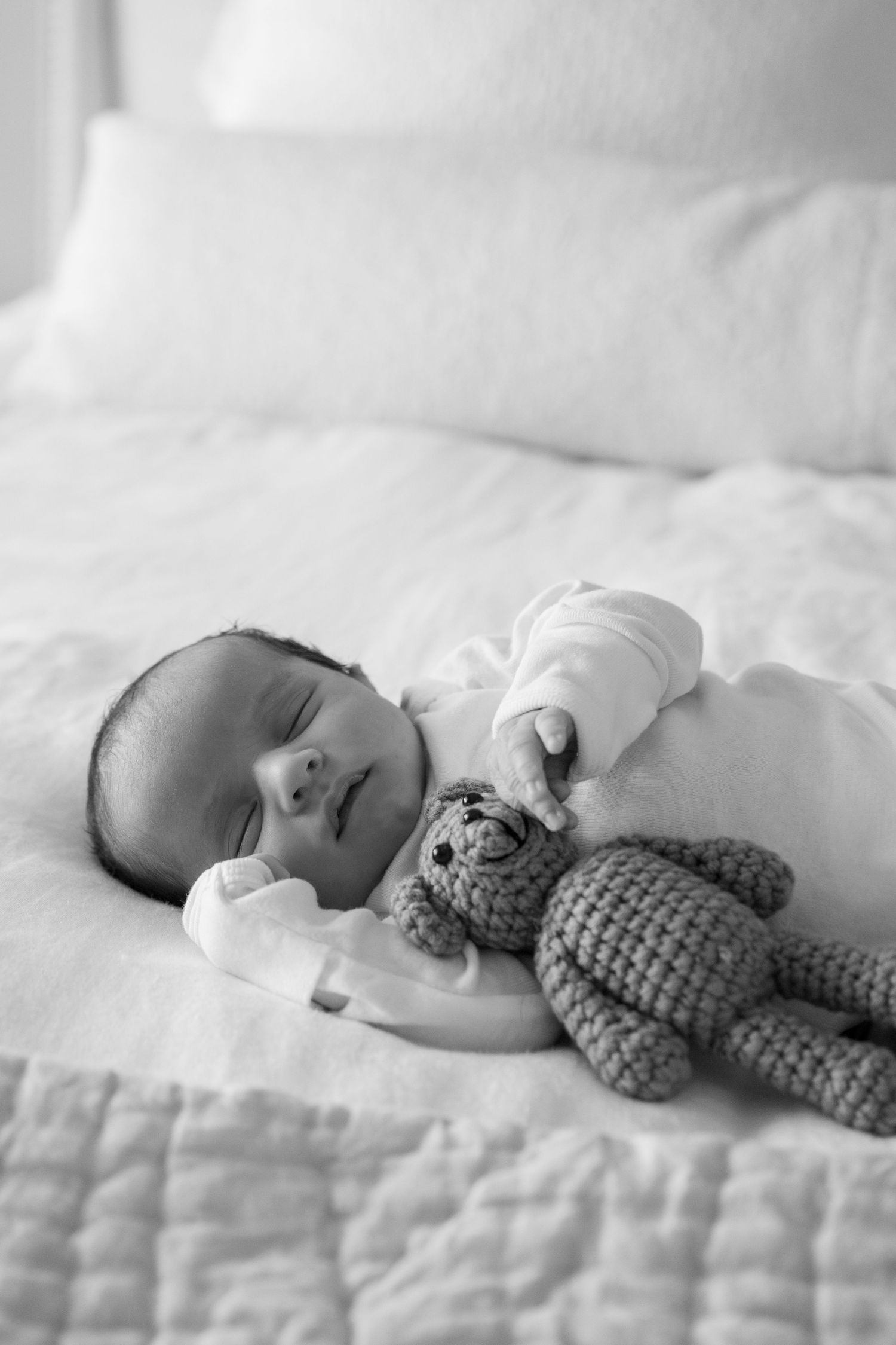 Sleeping baby in black and white photo with knitted toy on textured bedding.