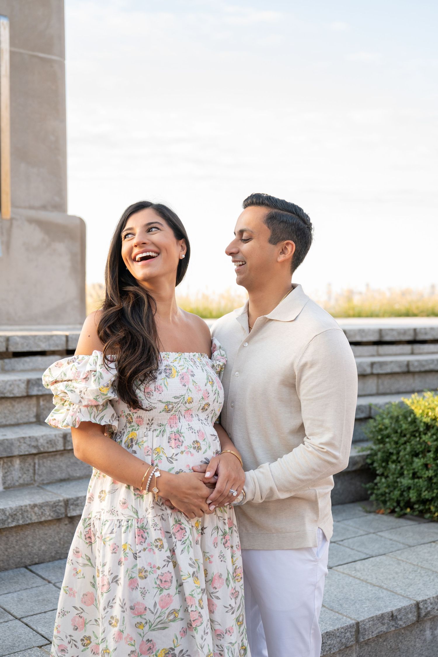 A couple shares a joyful moment together outdoors wearing coordinated white and floral outfits.